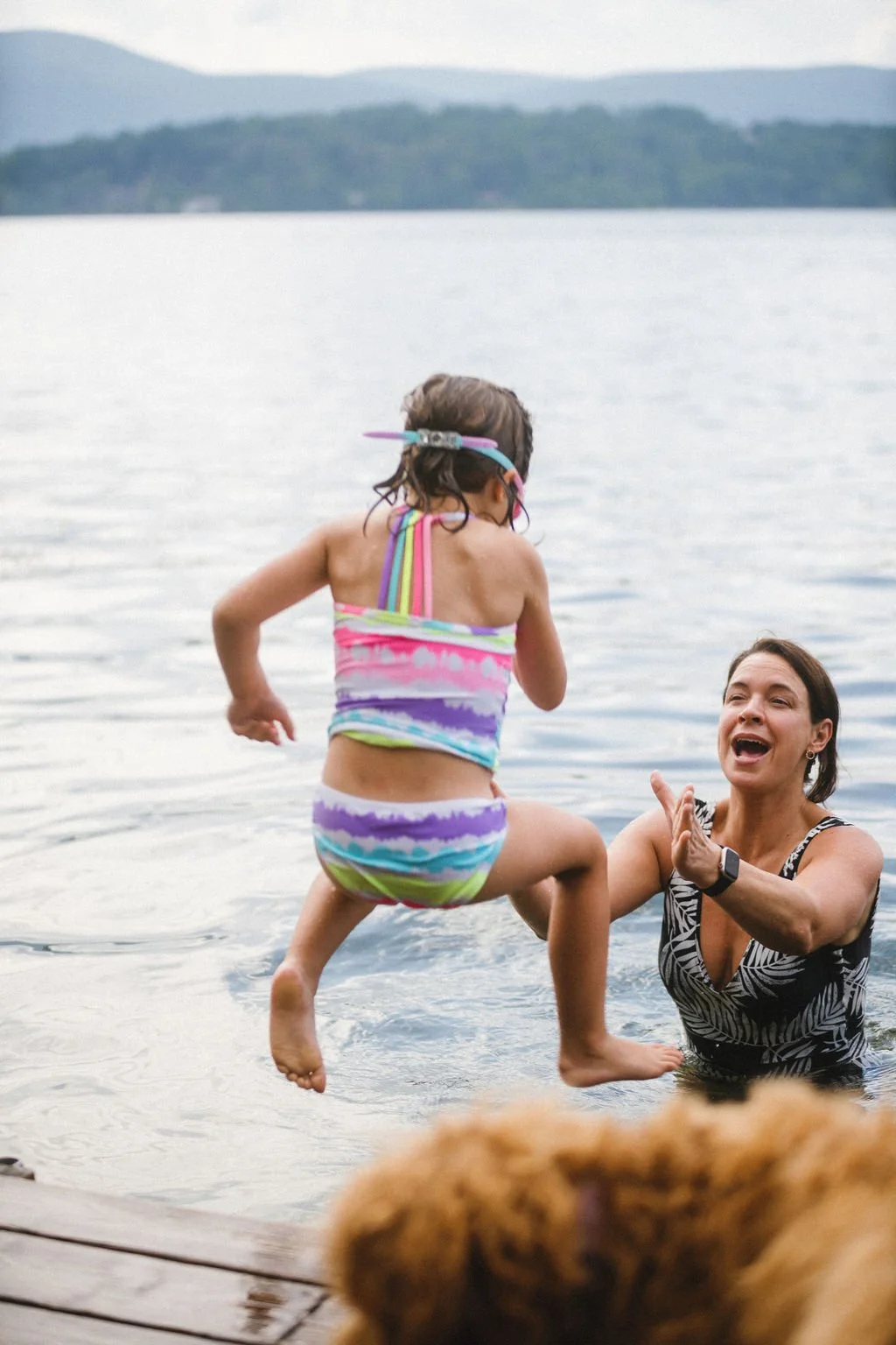 A woman playing in the water with a young girl at a lake, both smiling and enjoying the moment.