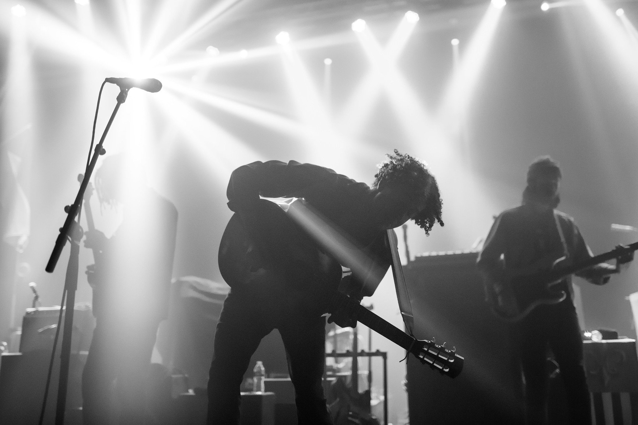 Lewis del Mar performing on stage with bright rays of light cutting through haze.