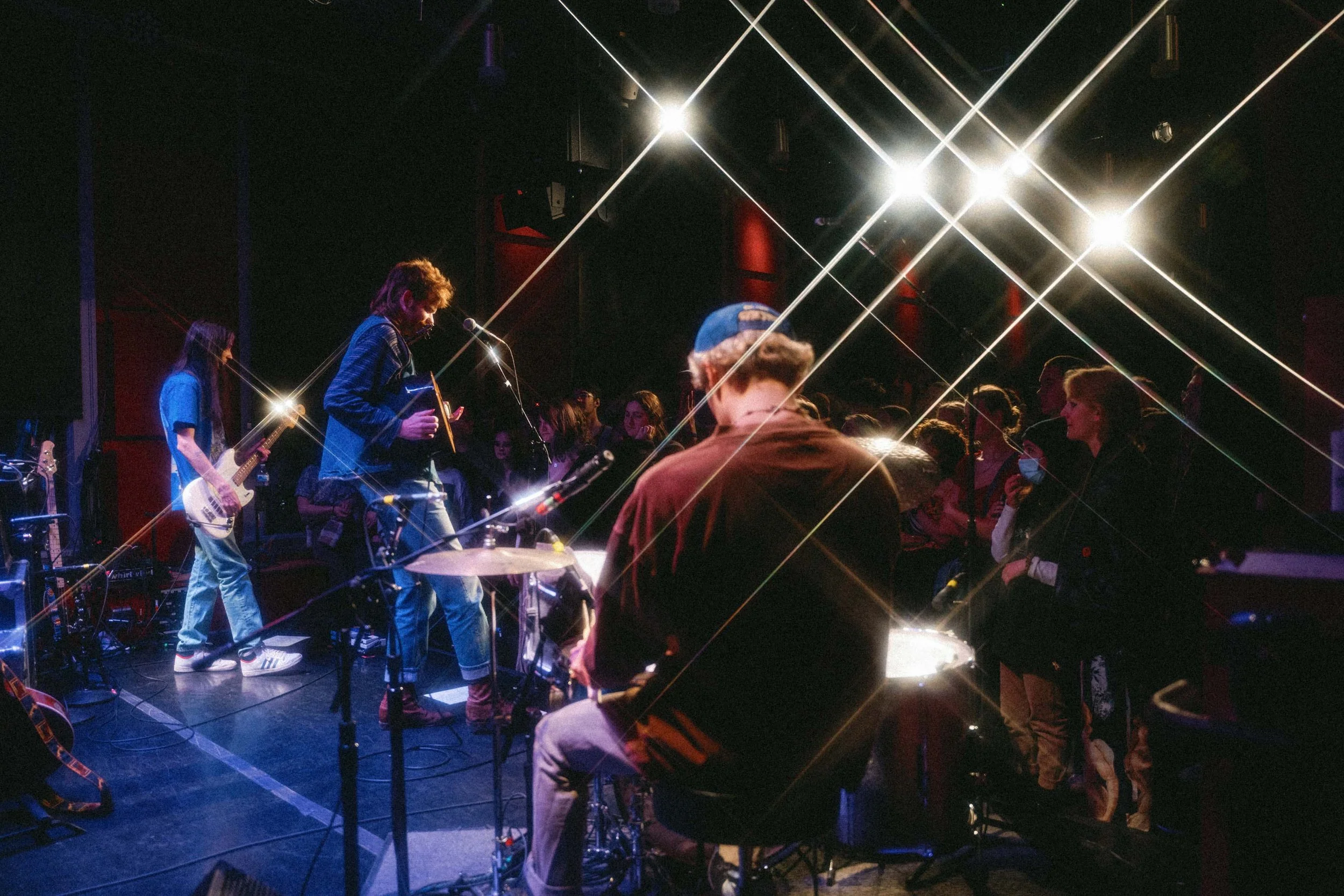 Musicians performing on stage with audience watching, stage lighting creates starburst effects.