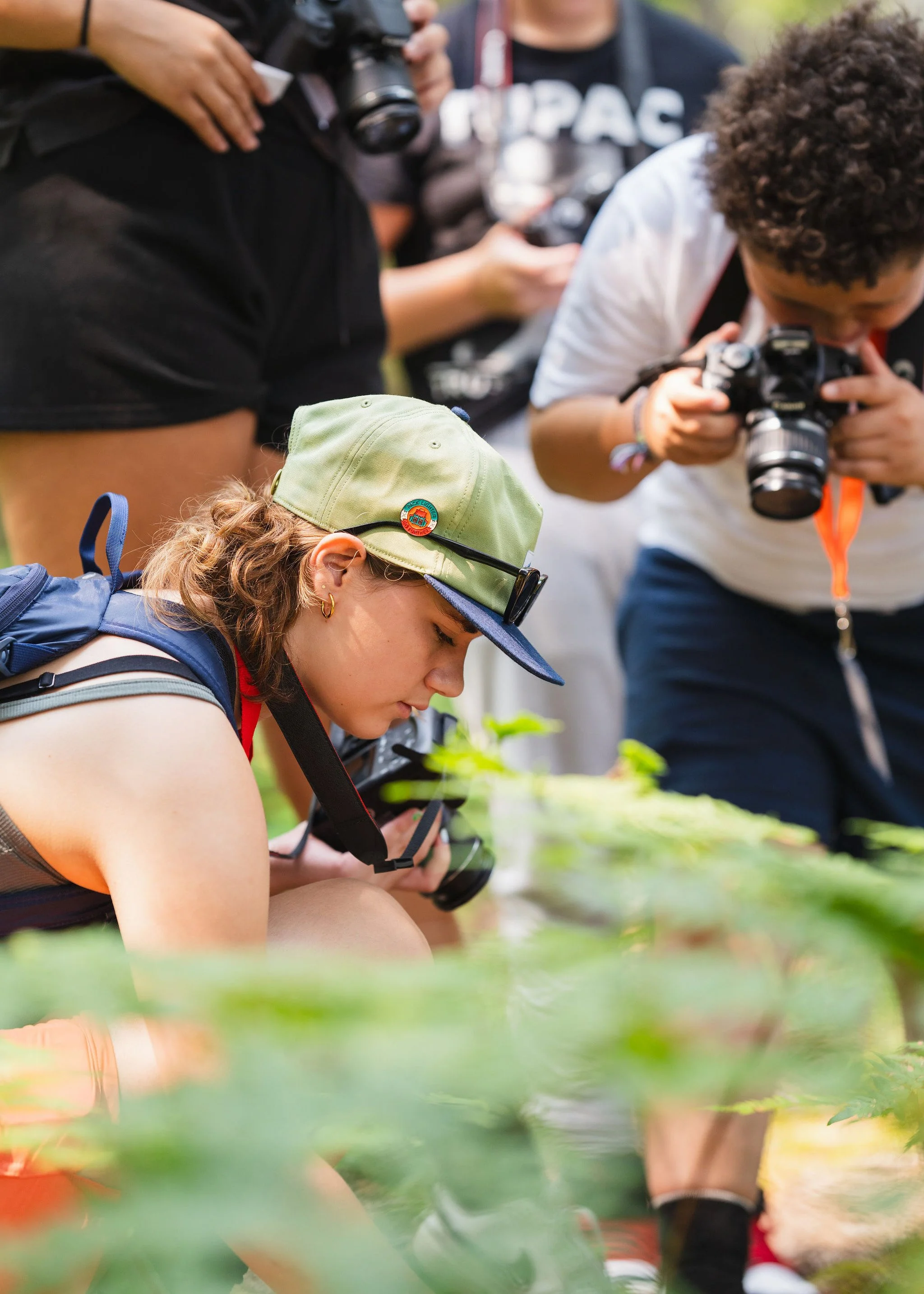 Group of young people closely observing plants outdoors, with some taking photographs.