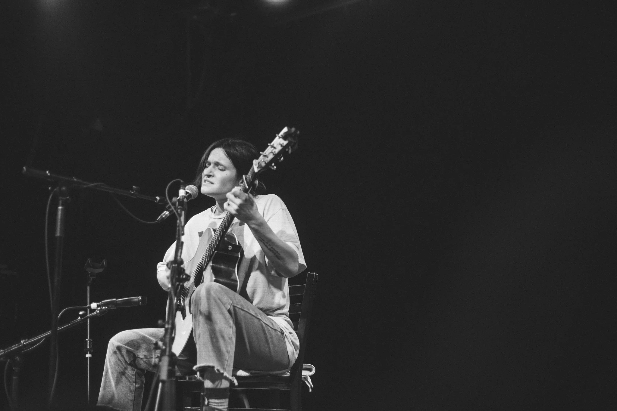 Adrianne Lenker singing and playing an acoustic guitar on stage, in black and white.