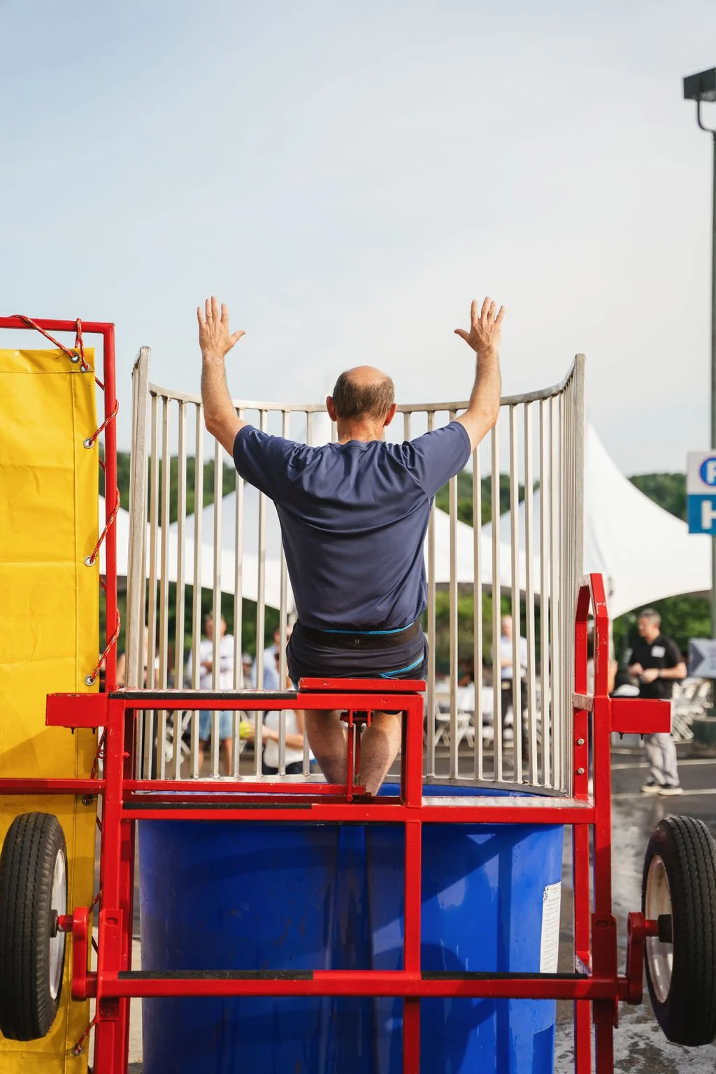 A man sitting on a zip line platform with his arms raised at an outdoor event.