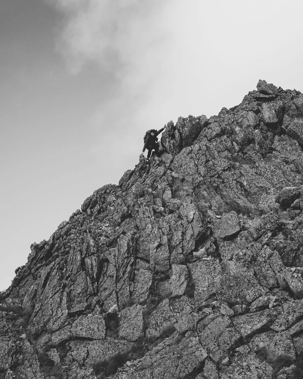 A person climbing a rugged, rocky mountain in black and white.