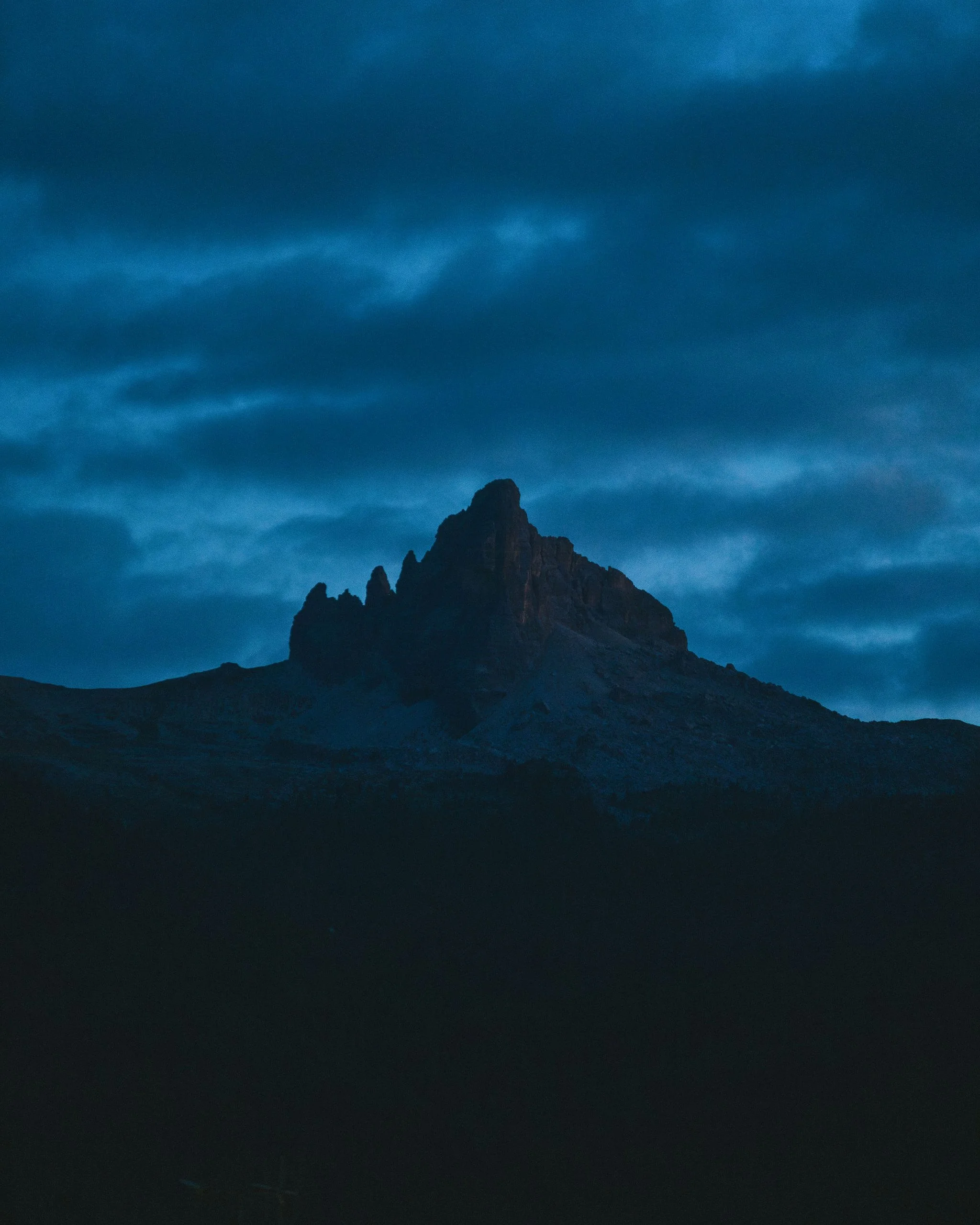 A mountain peak under a cloudy sky during twilight or dawn.