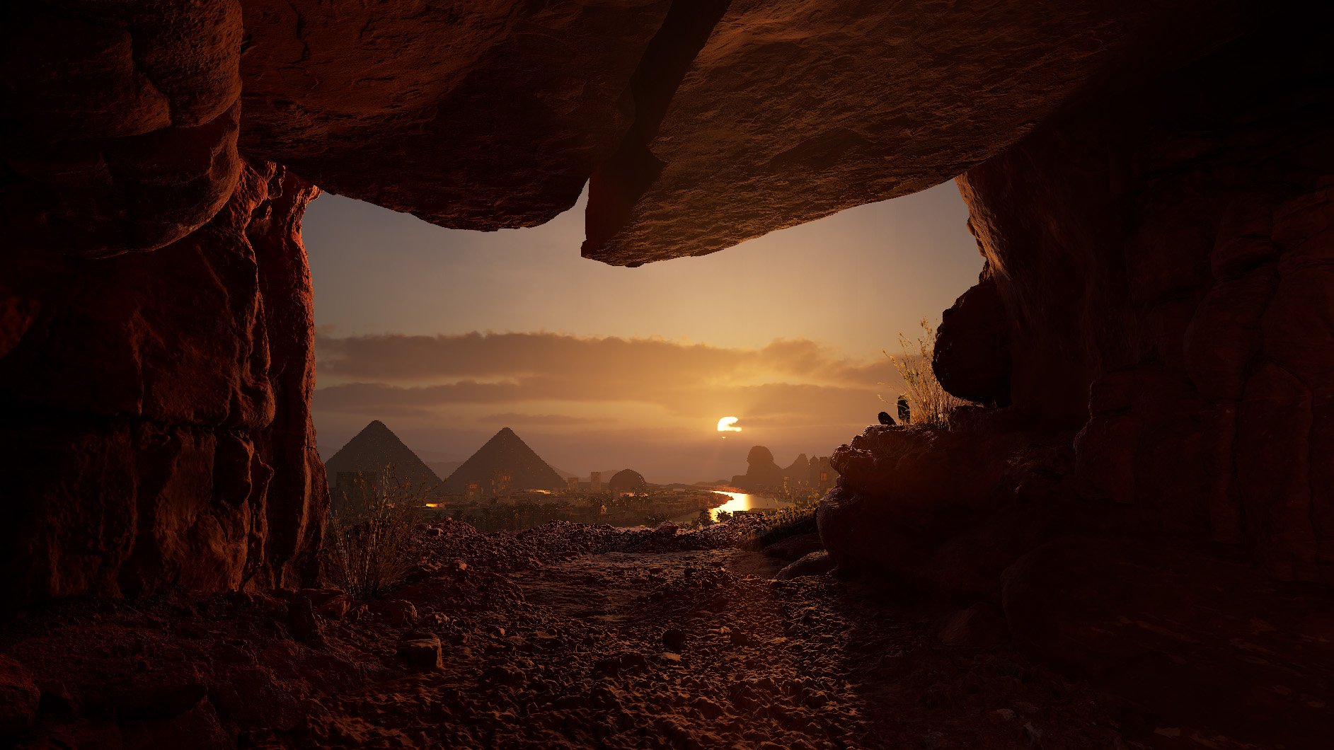 View of the pyramids and the Nile River at sunset, seen through a rocky cave opening.