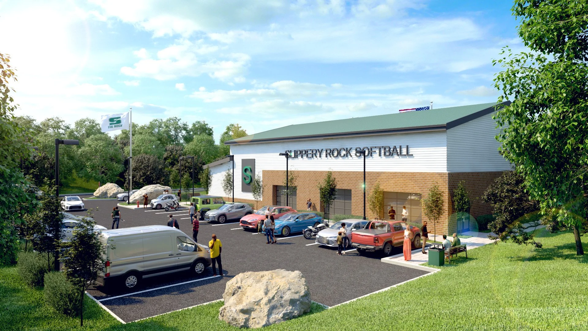 A modern softball facility with the sign 'Slippery Rock Softball' on the front of the building, a parking lot filled with cars, and people walking around and sitting outside on benches. The facility is surrounded by greenery and trees under a partly 