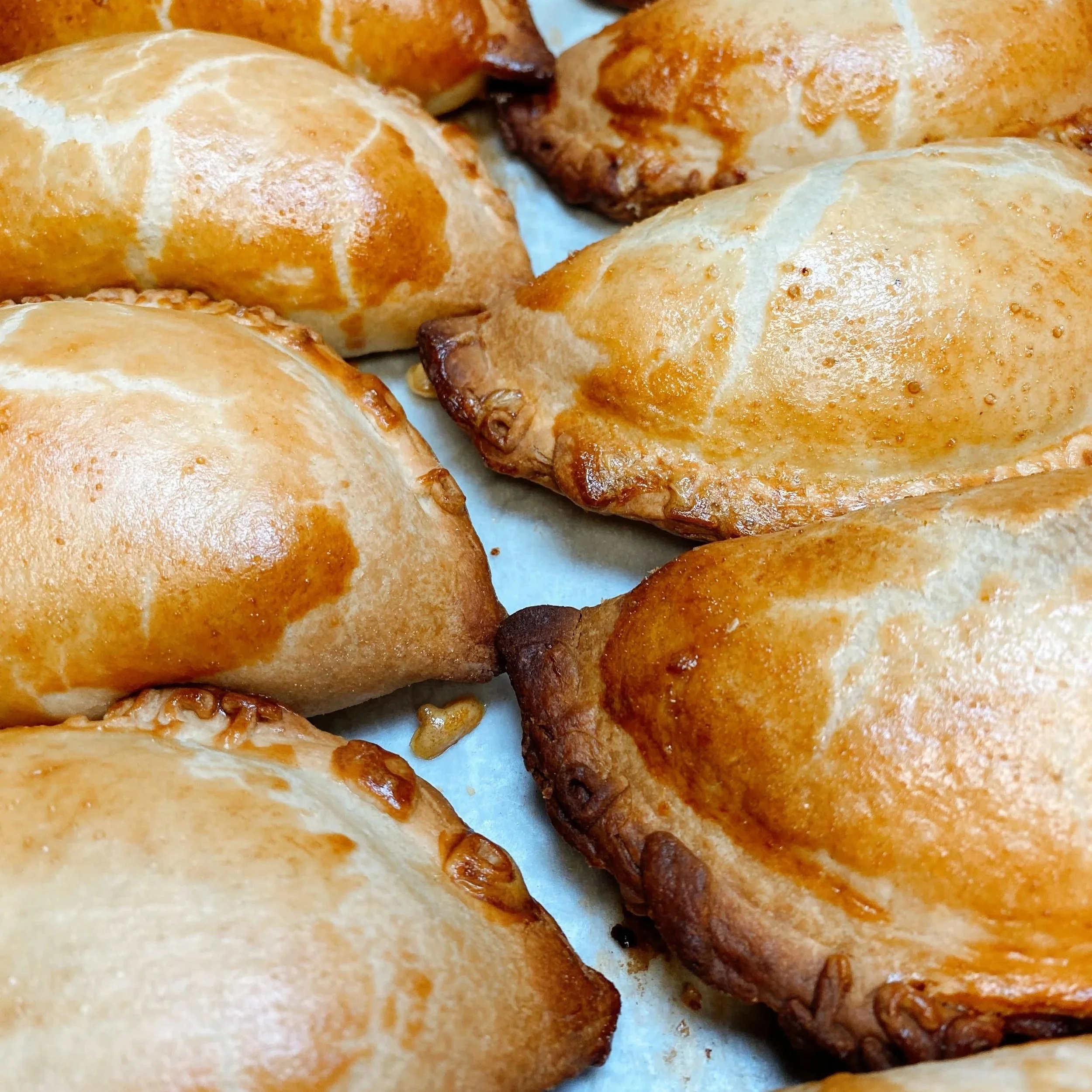 Close-up of baked empanadas with golden crusts on a baking sheet.