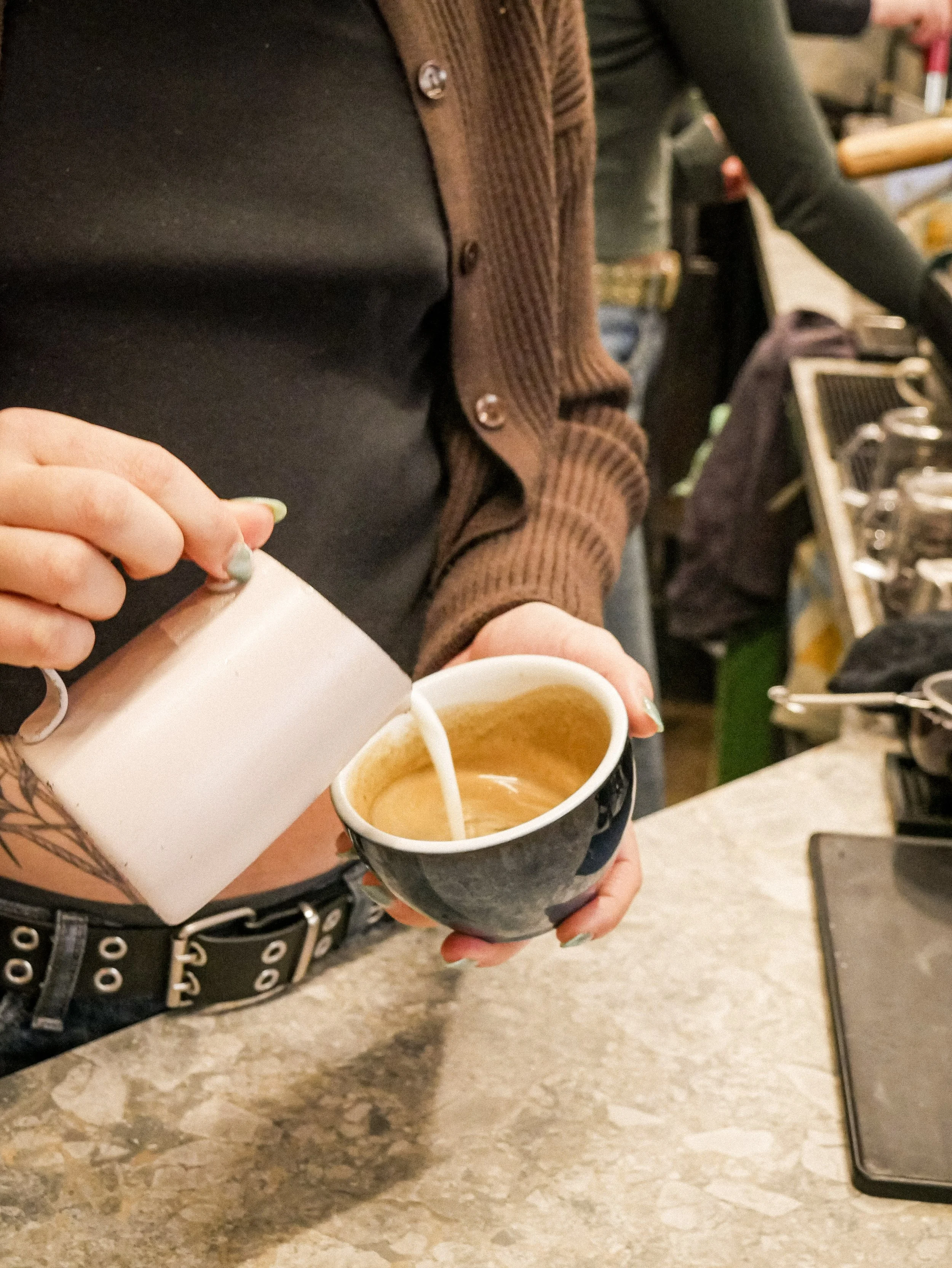 Person pouring milk into a cup of coffee in a coffee shop.