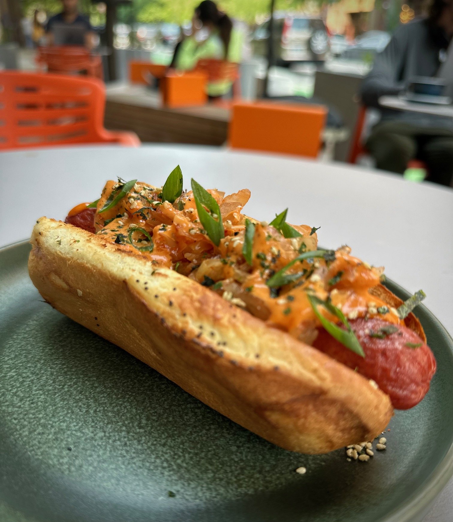 Seoul dog topped with green onions, and seasonings on a bun,.