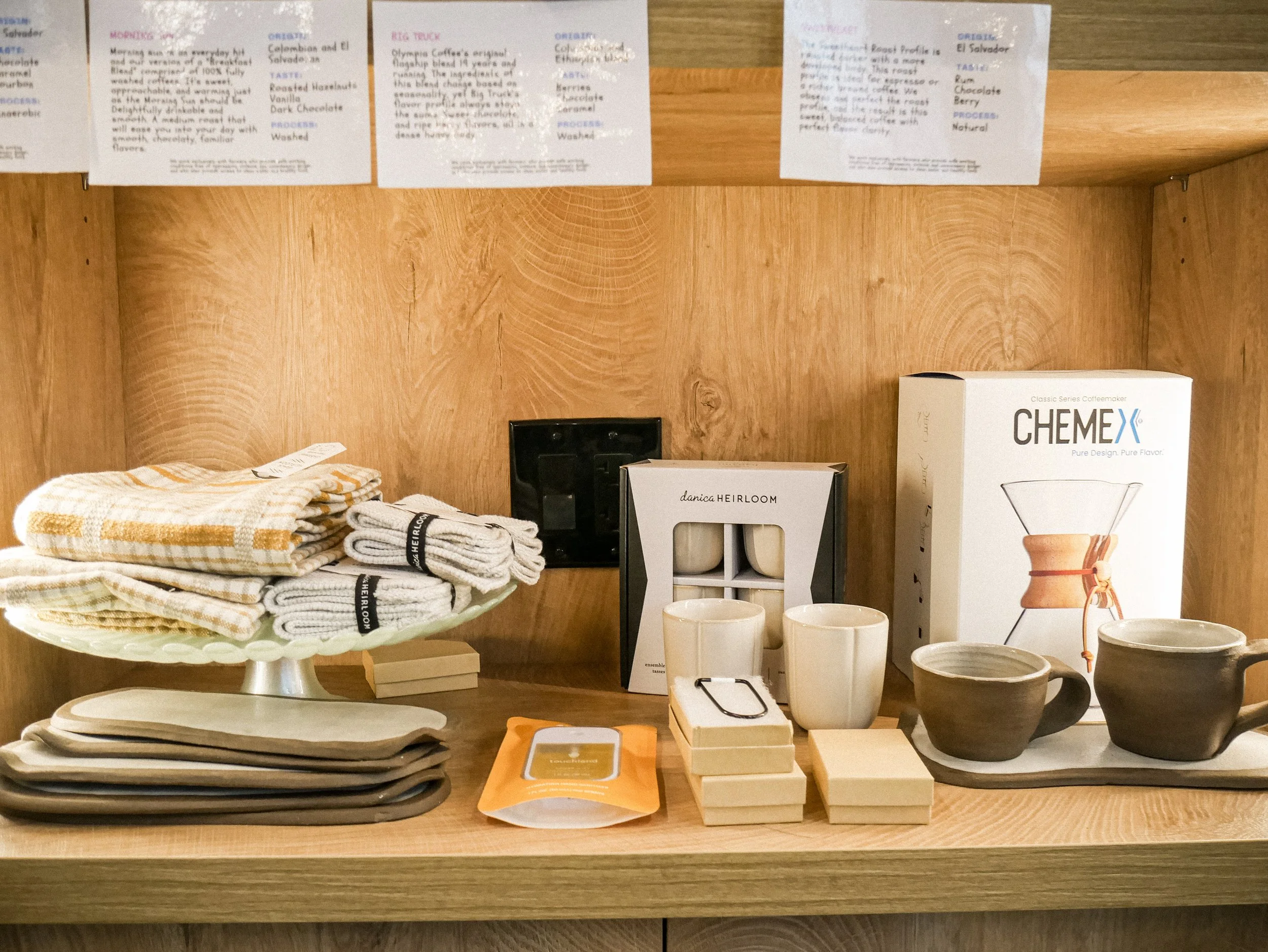 Display of various kitchen and dining items including towels, plates, candles, coasters, coffee drippers, cups, and bowls.