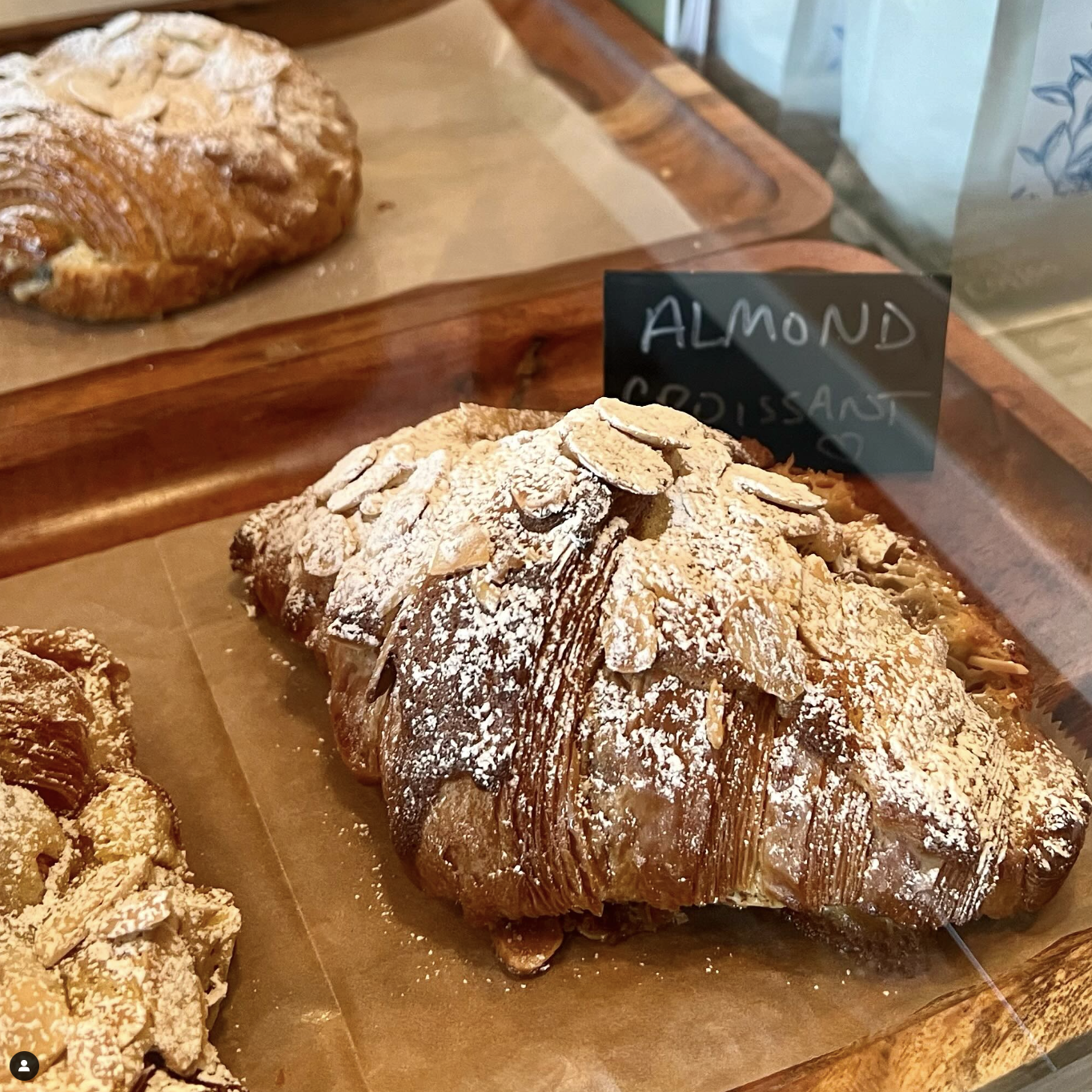 Almond croissant in a bakery display case with a sign that reads 'Almond' and sliced almonds on top.
