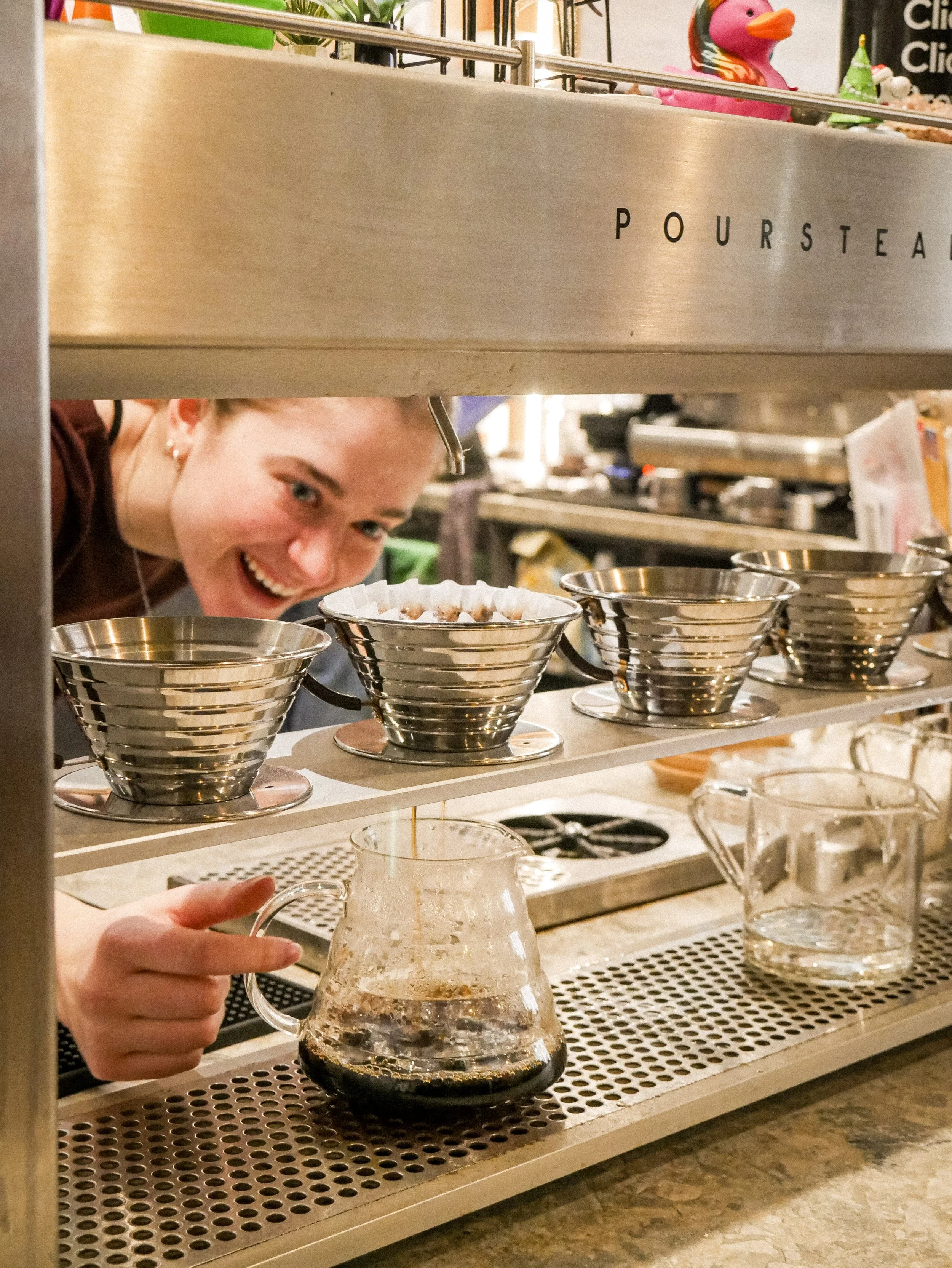 A woman smiling while pouring coffee from a poursteady pourover machine