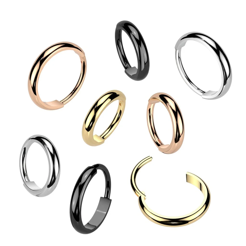 Collection of nine metallic rings in gold, silver, black, and rose gold finishes, arranged in a scattered pattern against a white background.