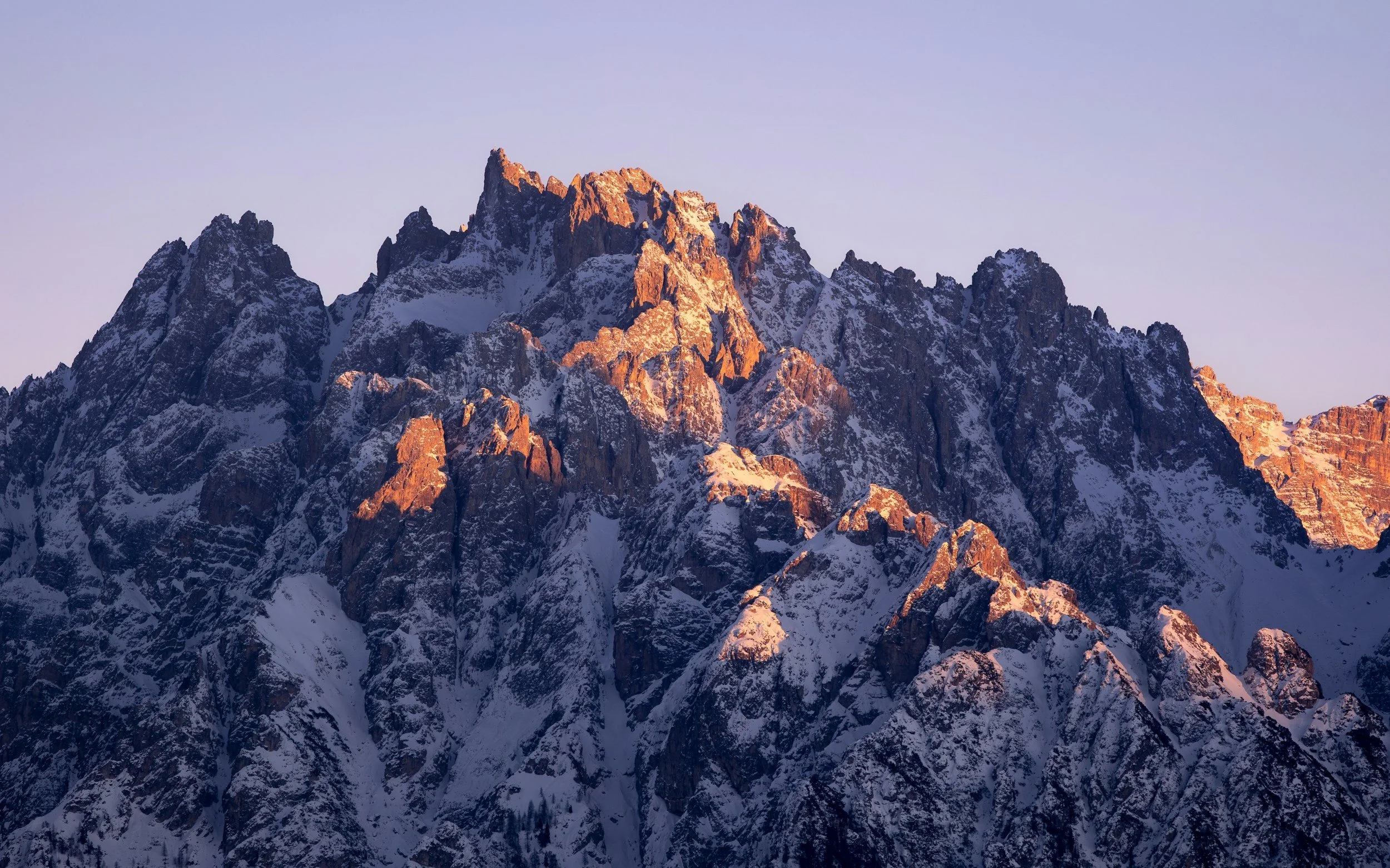 Snow-capped mountain peaks illuminated by sunlight with a clear sky in the background.