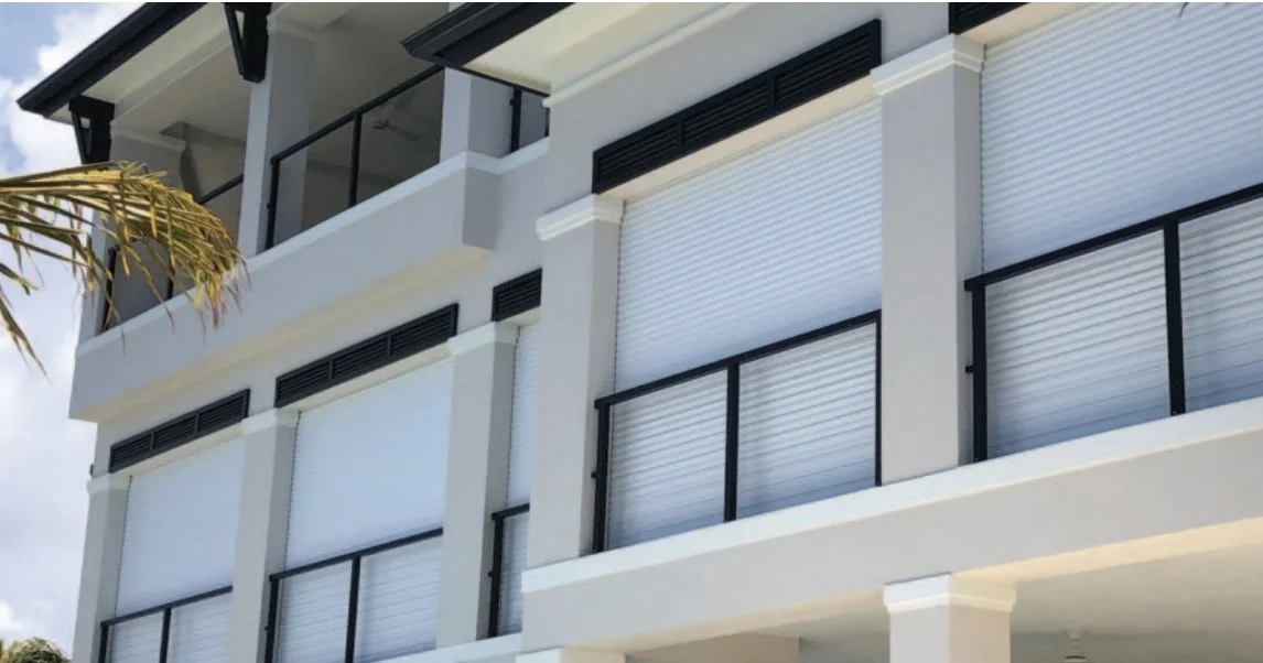 Modern building with white walls, black window frames, and closed white window shutters in a sunny location.