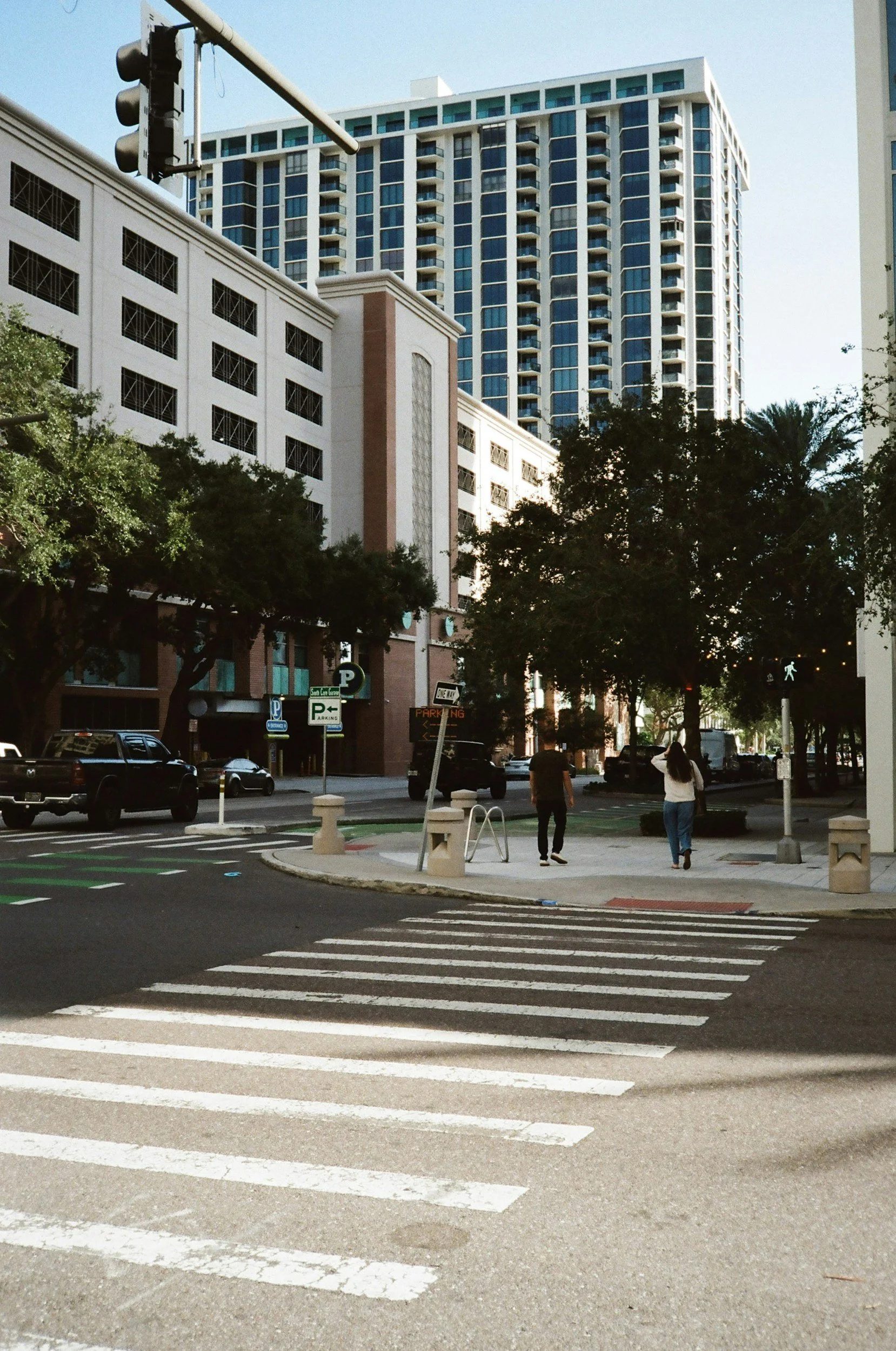 Urban city scene with tall buildings, a crosswalk, and pedestrians walking on the sidewalk during daytime.