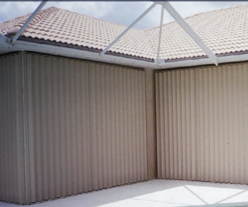 Partially open corner of an outdoor patio with beige vertical blinds and a tiled roof overhead.