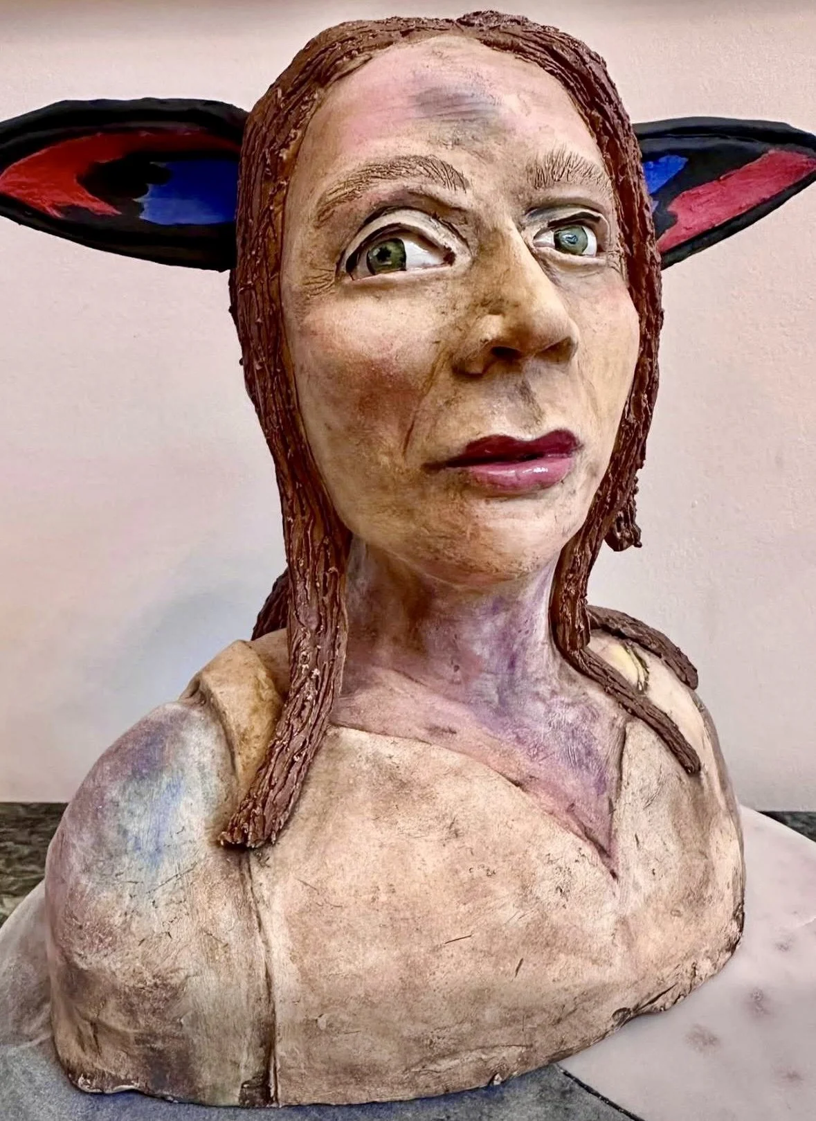 A sculpture of a woman with light skin, large eyes, and brown hair, wearing black and red butterfly or fairy wings.