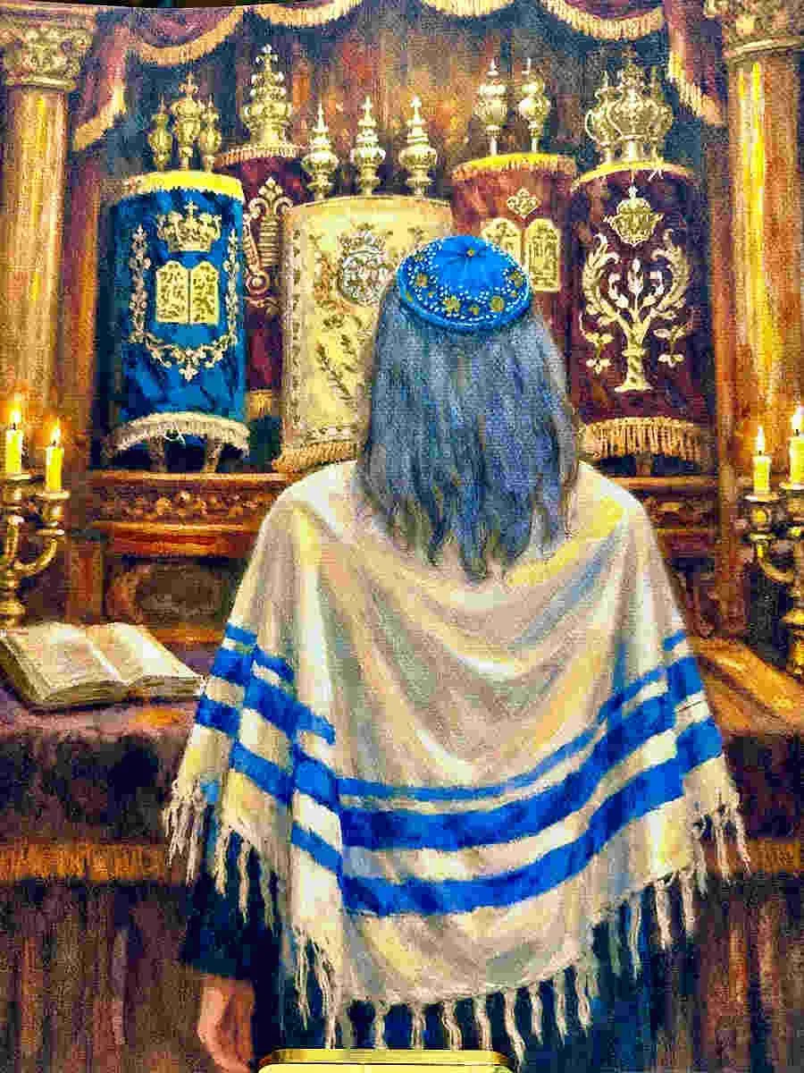Person standing before an ornate Jewish prayer wall, wearing a tallit and a kippah with stars and moon design, in a religious setting surrounded by candles and religious banners.