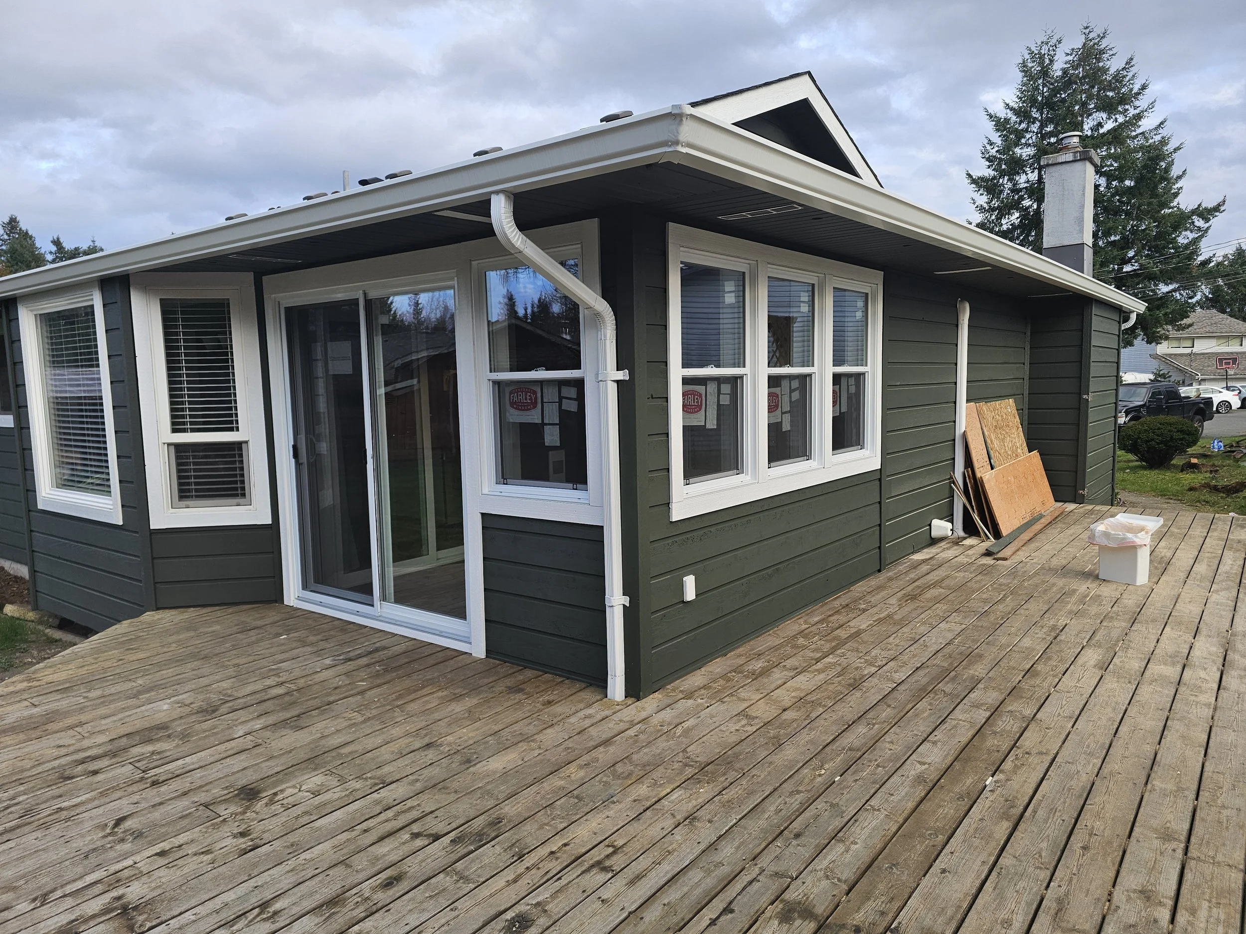 Exterior house painting project in Campbell River – freshly painted green siding with white trim and new wooden deck