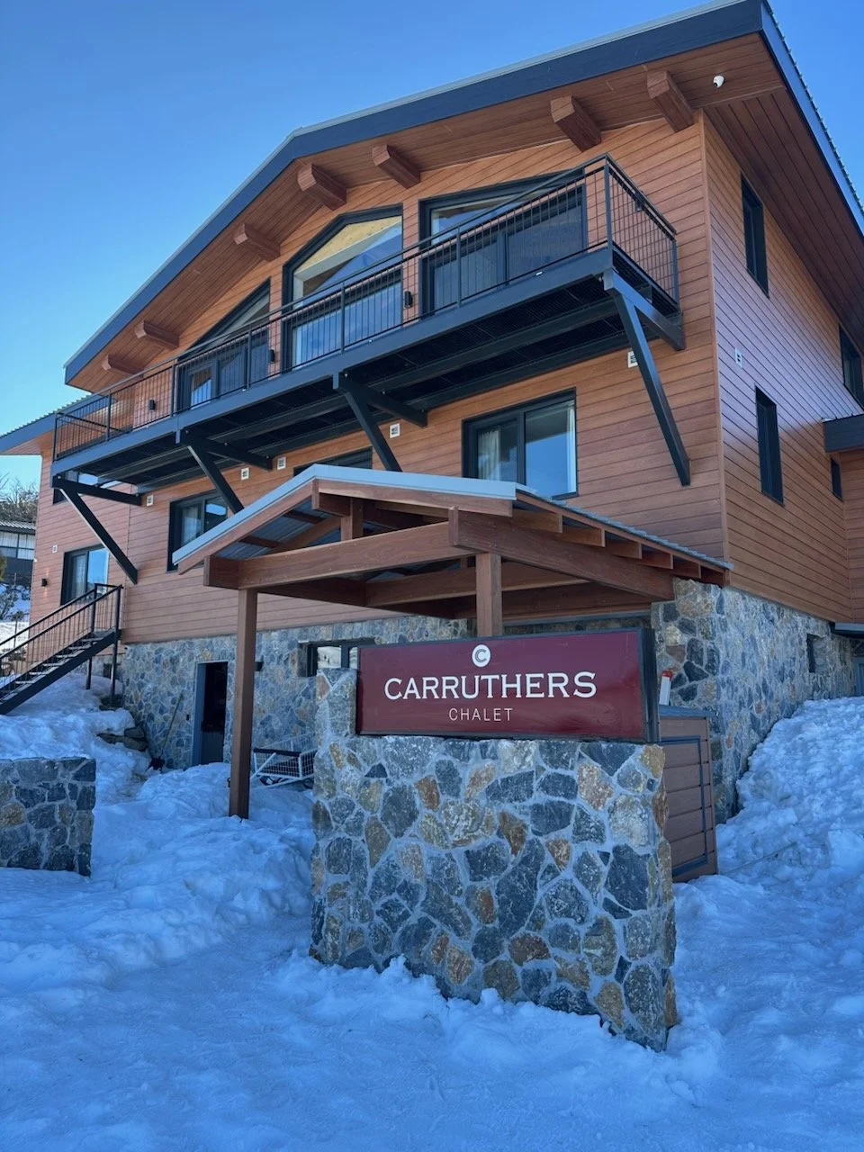 A multi-story wooden chalet named Carruthers Chalet with stone foundation, located in a snowy area.