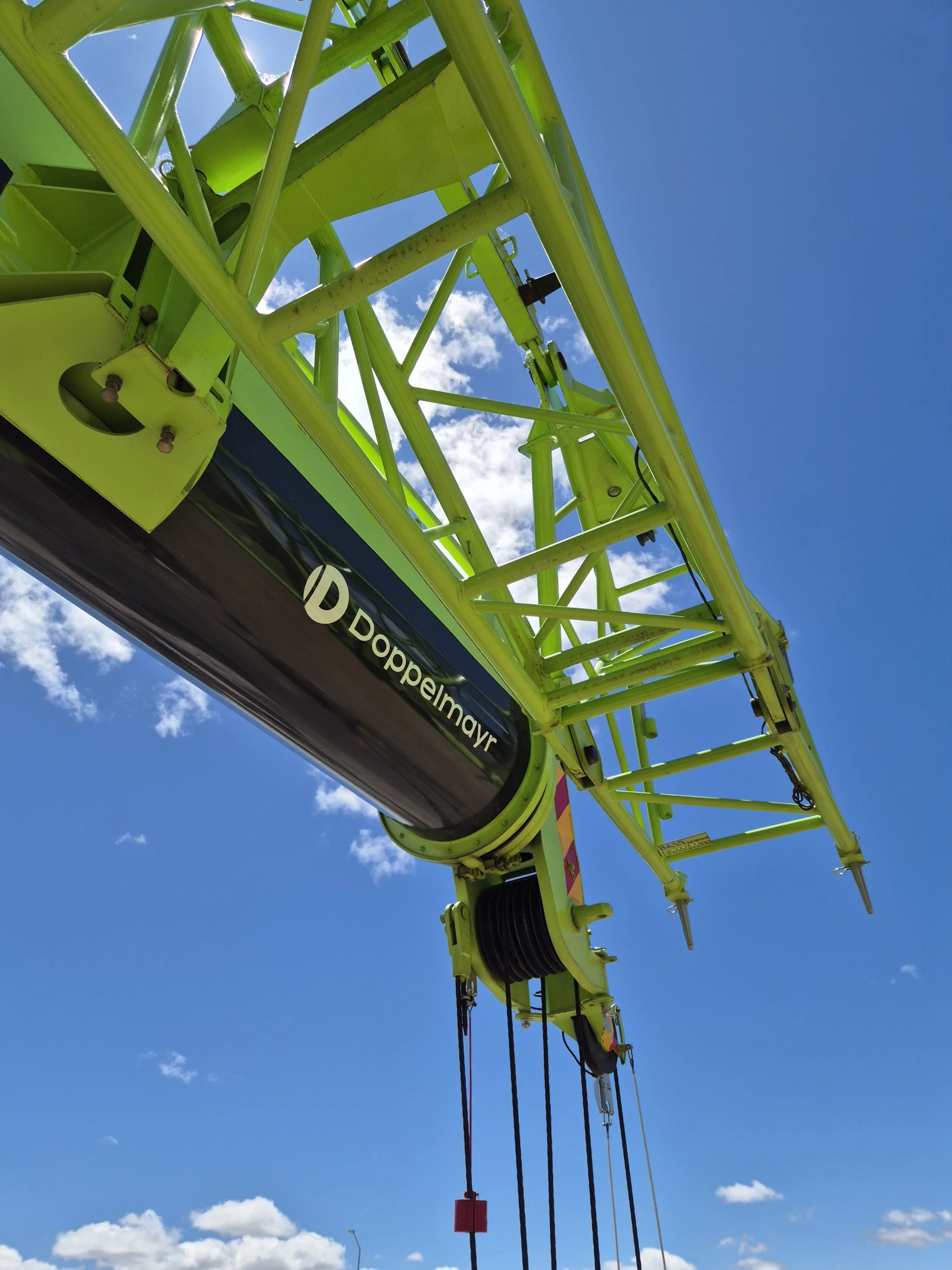 Close-up of a bright yellow-green crane with the brand name 'Doppelmayr' on a black component, set against a blue sky with scattered white clouds.