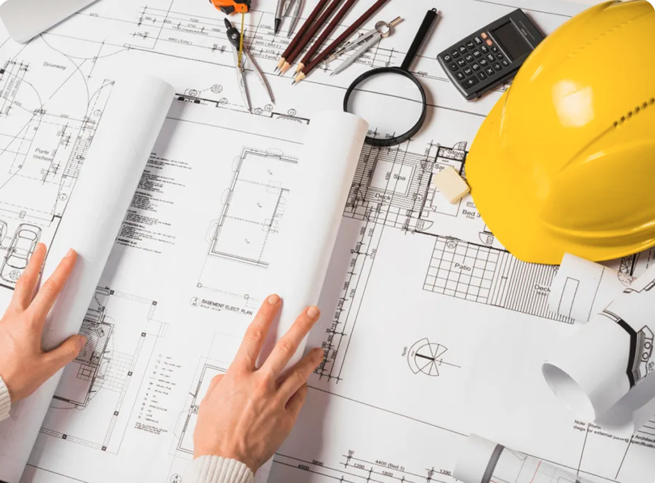 Architectural blueprints on a table with tools, a yellow hard hat, and a calculator.