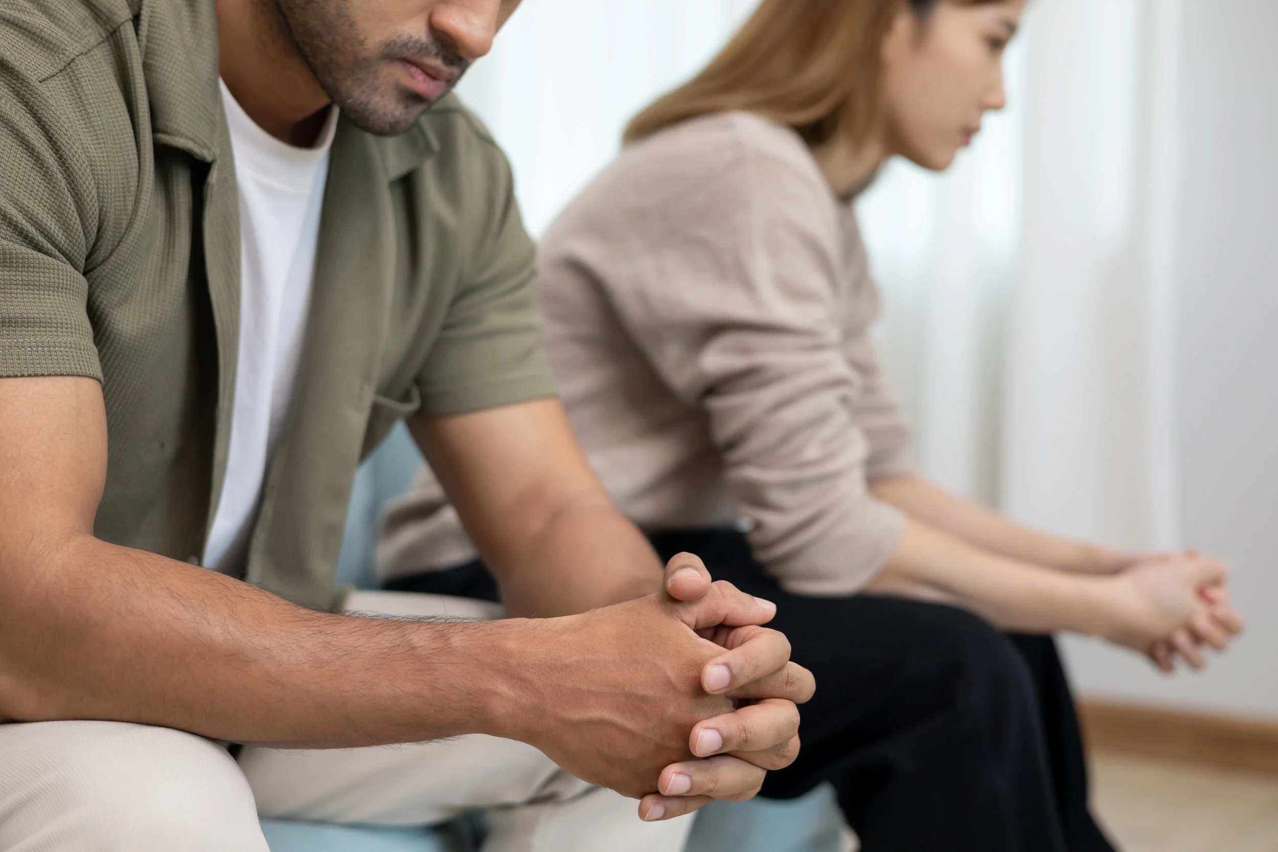 Two people sitting with hands clasped in prayer or meditation, eyes closed, in a calm setting.