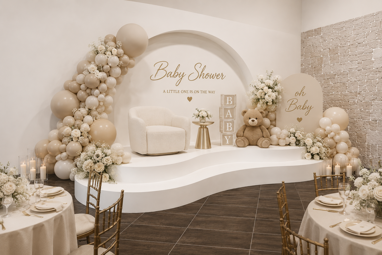 Decorated baby shower stage with white and beige balloons, flowers, a teddy bear, and blocks spelling BABY, with a round table of place settings in the foreground.
