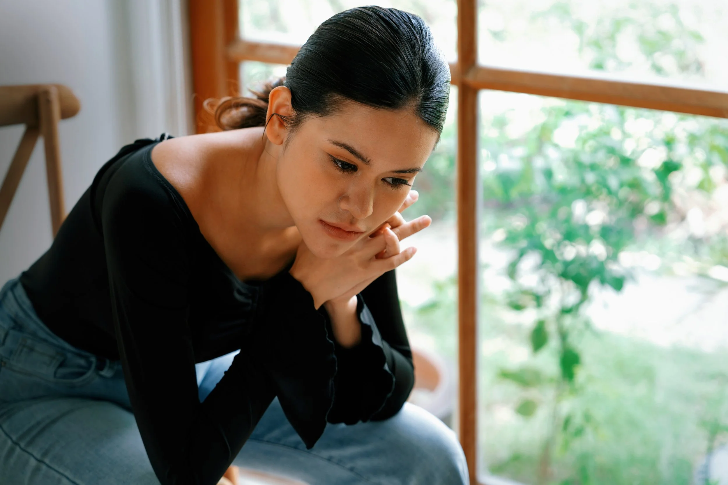 Woman sitting quietly with a thoughtful expression, reflecting emotional overload and mental strain