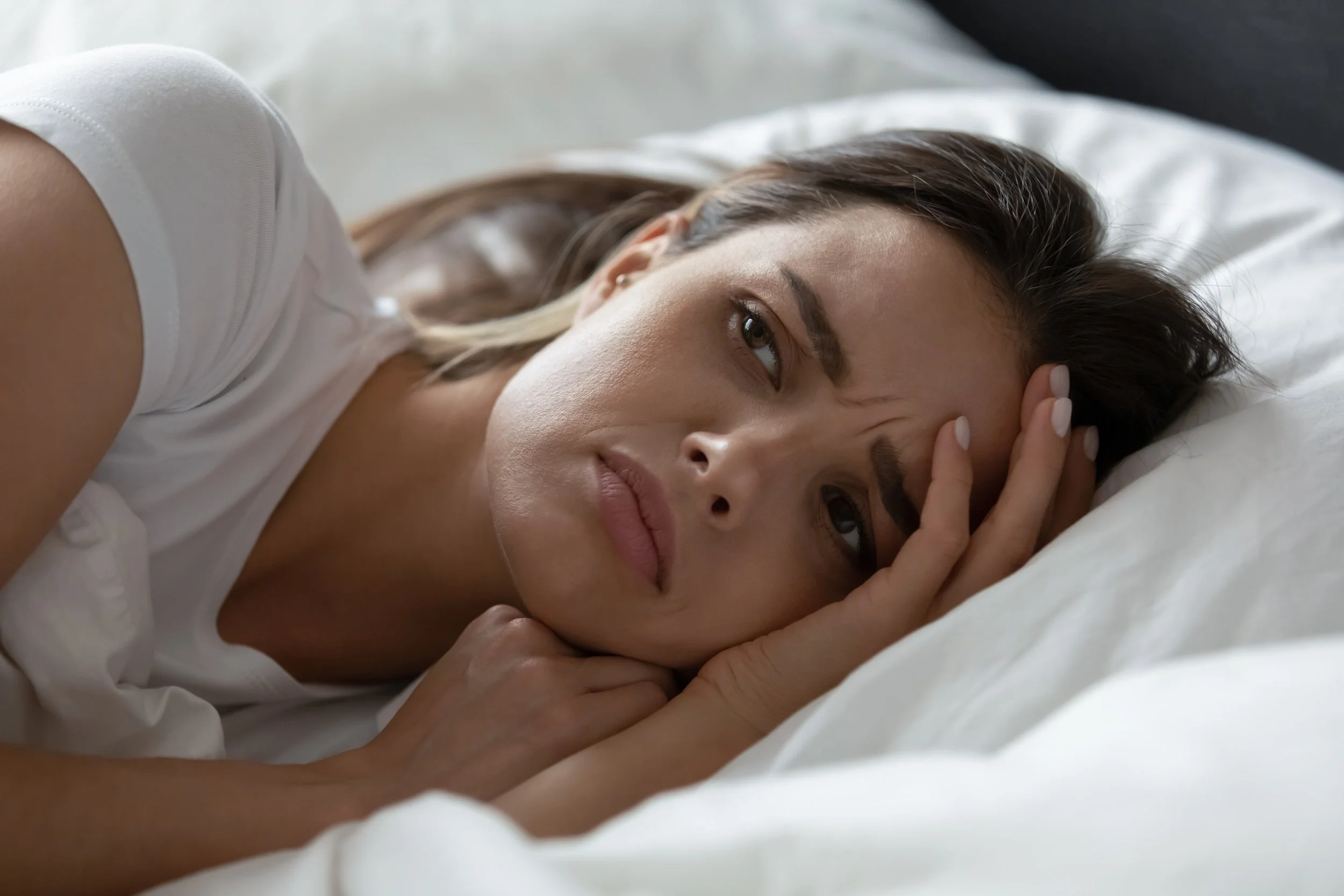 Woman lying awake in bed, reflecting quiet fatigue and emotional exhaustion related to sleep disruption