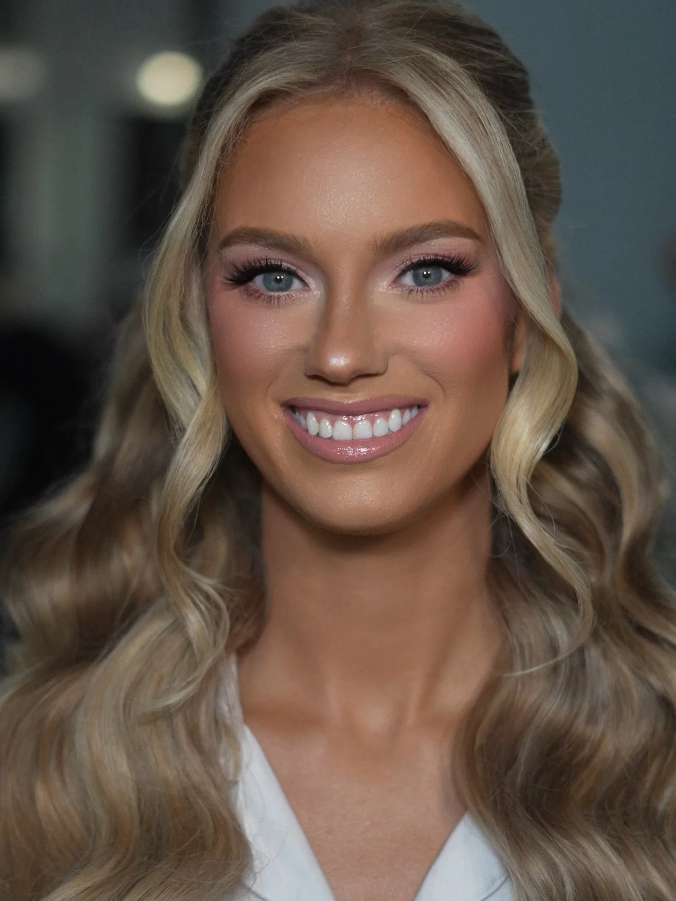 Close-up of a smiling woman with long, wavy blonde hair, blue eyes, and wearing light makeup.
