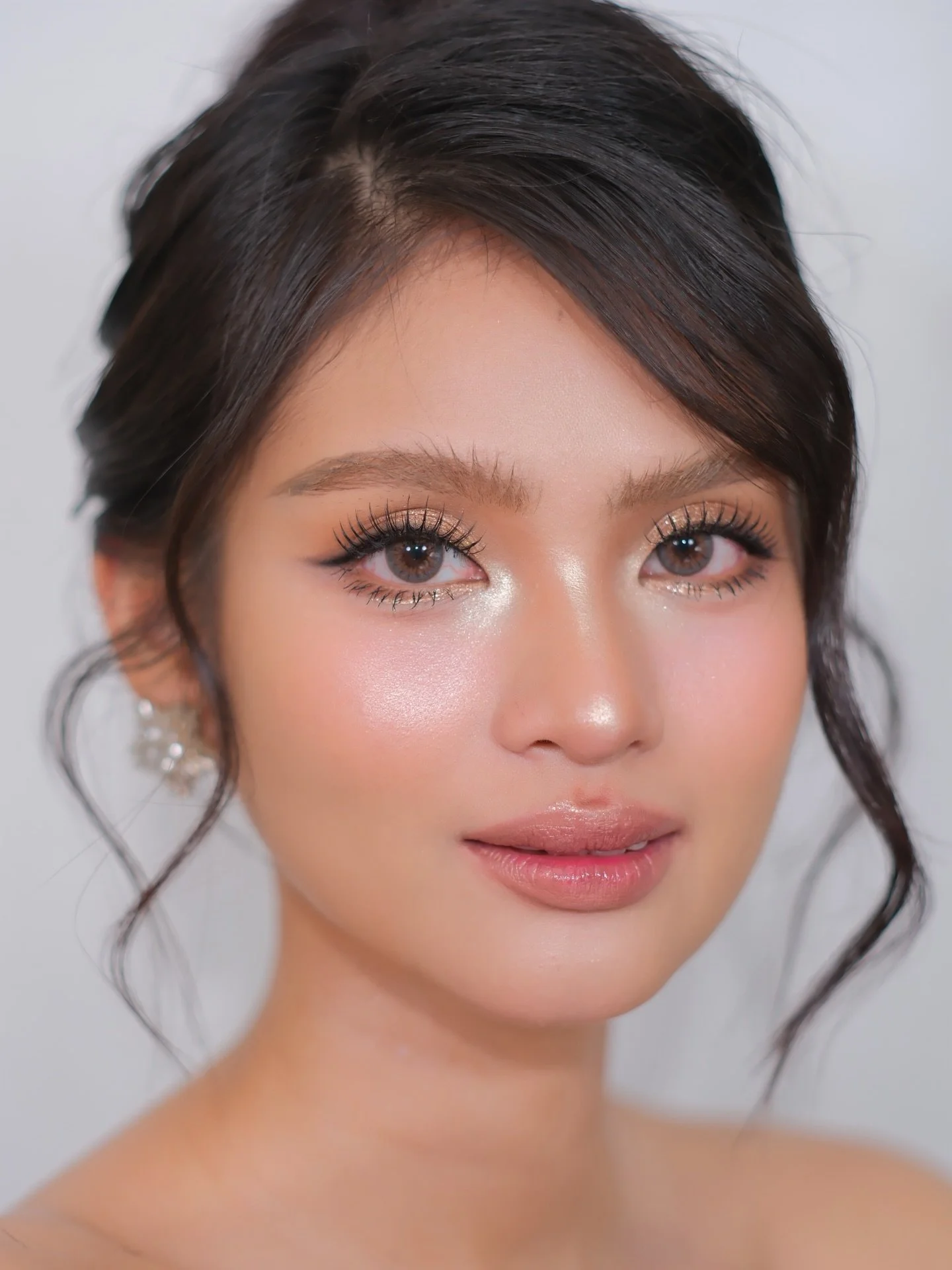 Close-up of a woman with styled dark hair, subtle makeup, and jewelry, looking at the camera.