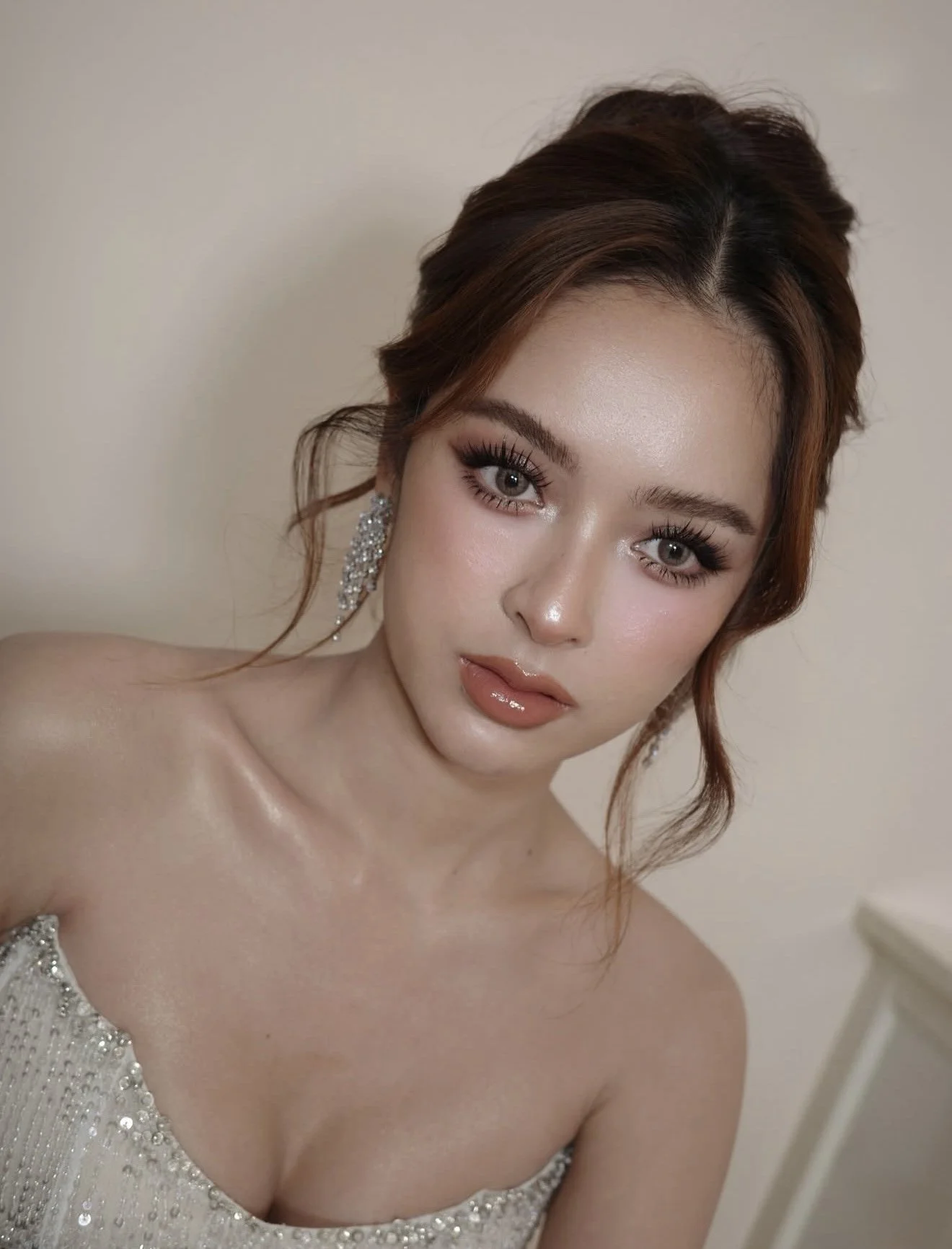 A woman with brown hair styled in loose waves, wearing makeup with emphasized eyes and lips, diamond earrings, and a strapless, sequined dress with beaded embellishments.