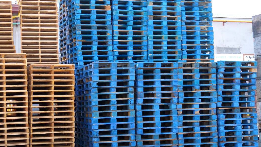 Stacked blue and brown wooden pallets at a warehouse or storage yard.