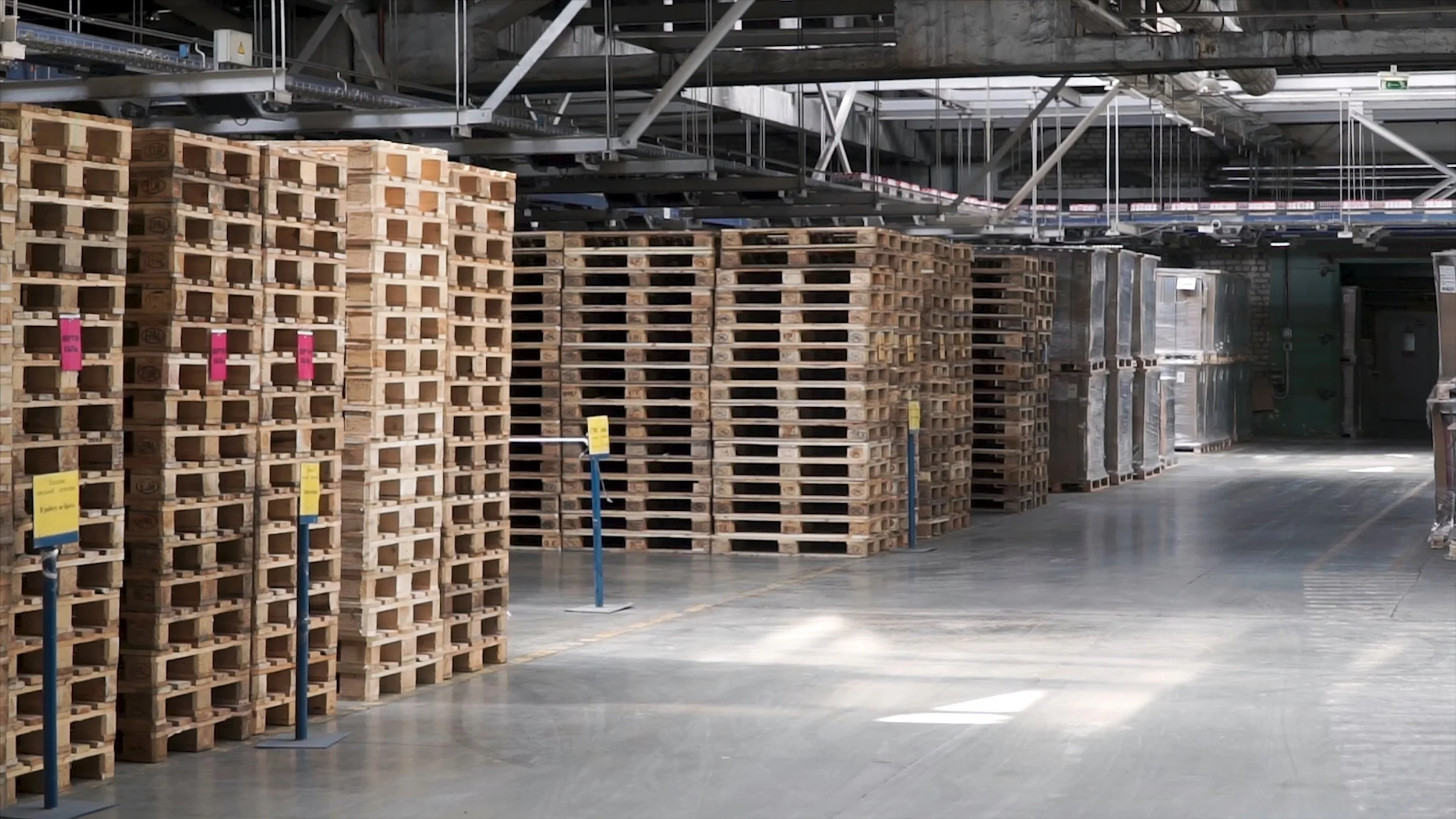 Stacks of wooden pallets inside a warehouse with a high ceiling and industrial lighting