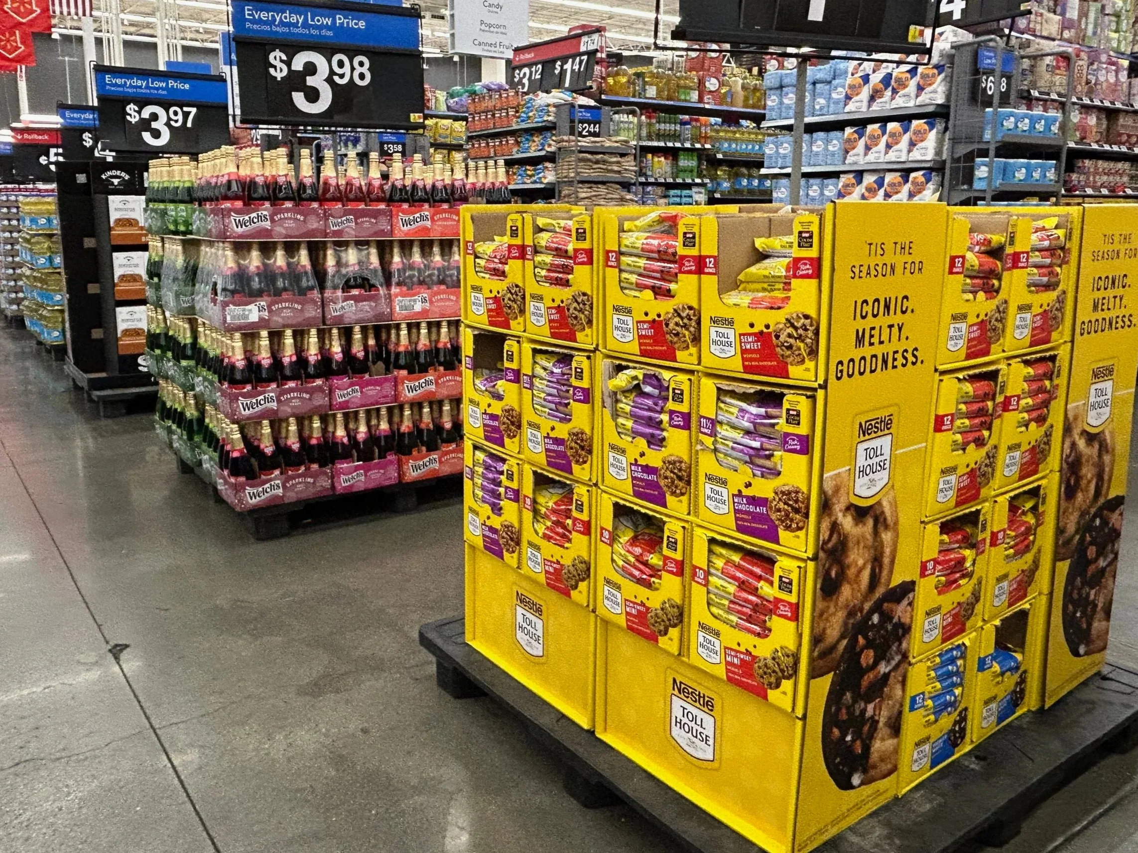Display of Welch's sparkling juice bottles on a pallet in a grocery store aisle with other snack items visible in the background.