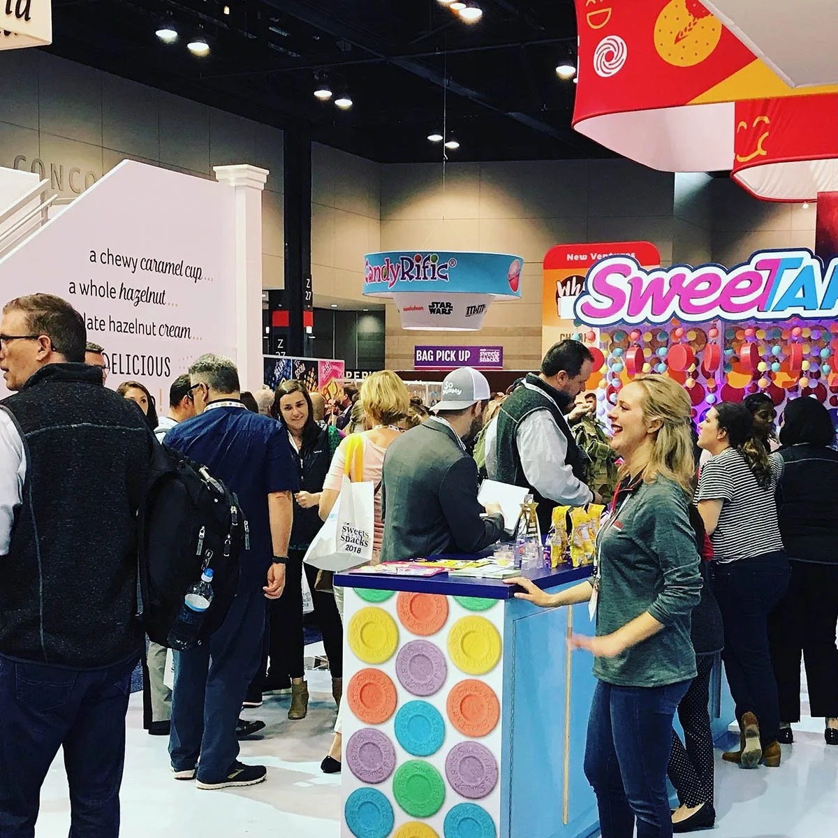 People at a candy booth with colorful decorations, signs, and advertisements at a convention or expo.