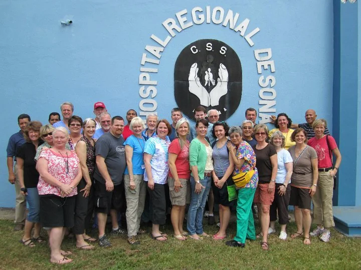 Group of people standing in front of a hospital regional design sign on a blue building.