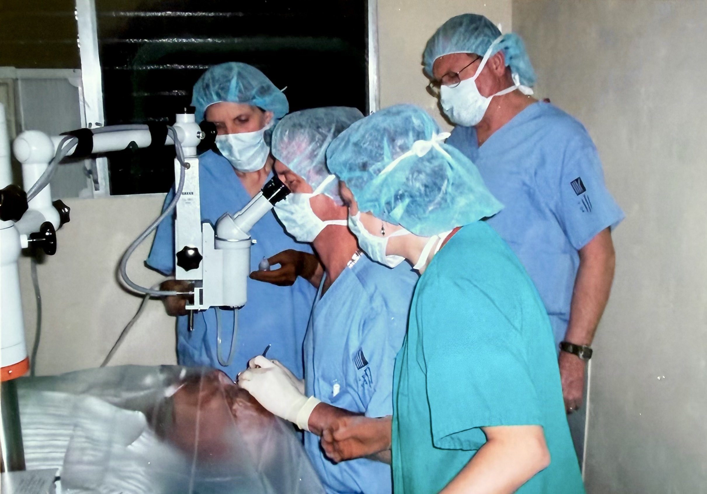 Medical professionals in scrubs, masks, and hair covers performing a medical procedure on a patient in a hospital operating room.