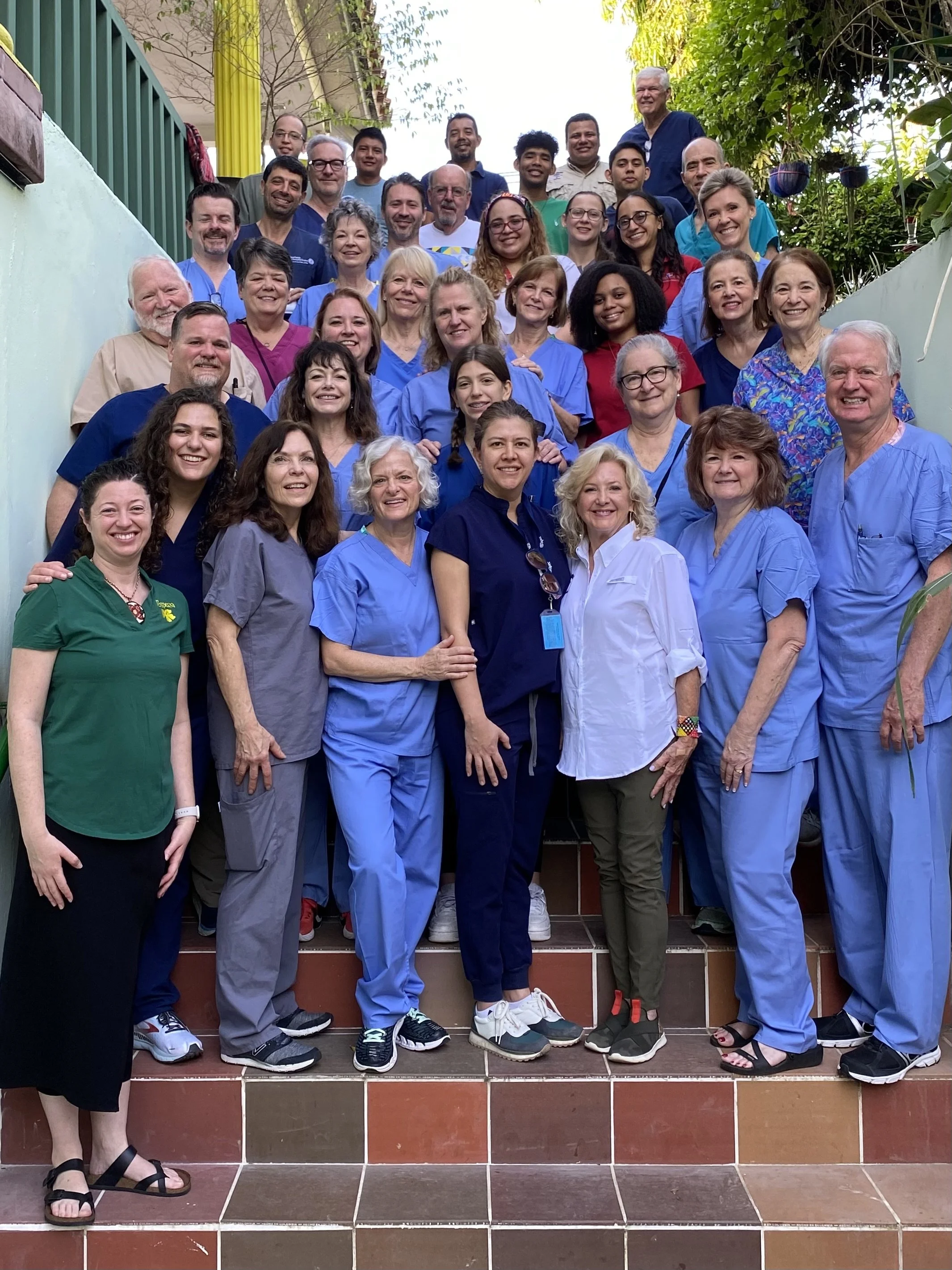 Group of diverse healthcare professionals and staff members gathered on stairs outdoors, smiling for a group photo.