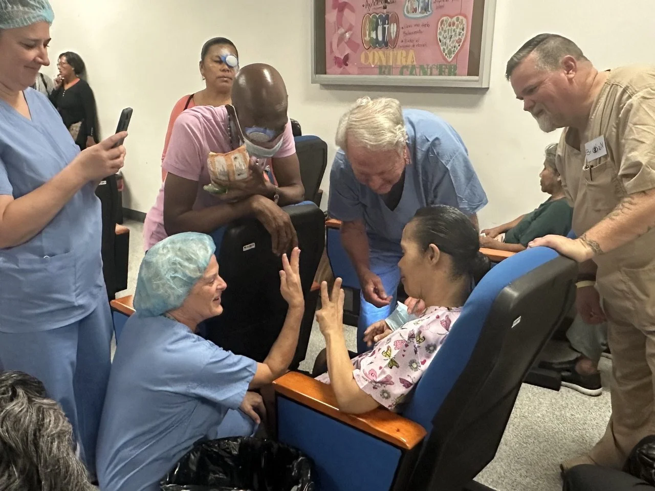 Group of healthcare workers and patients in a hospital waiting area, engaging in conversation and taking photos.