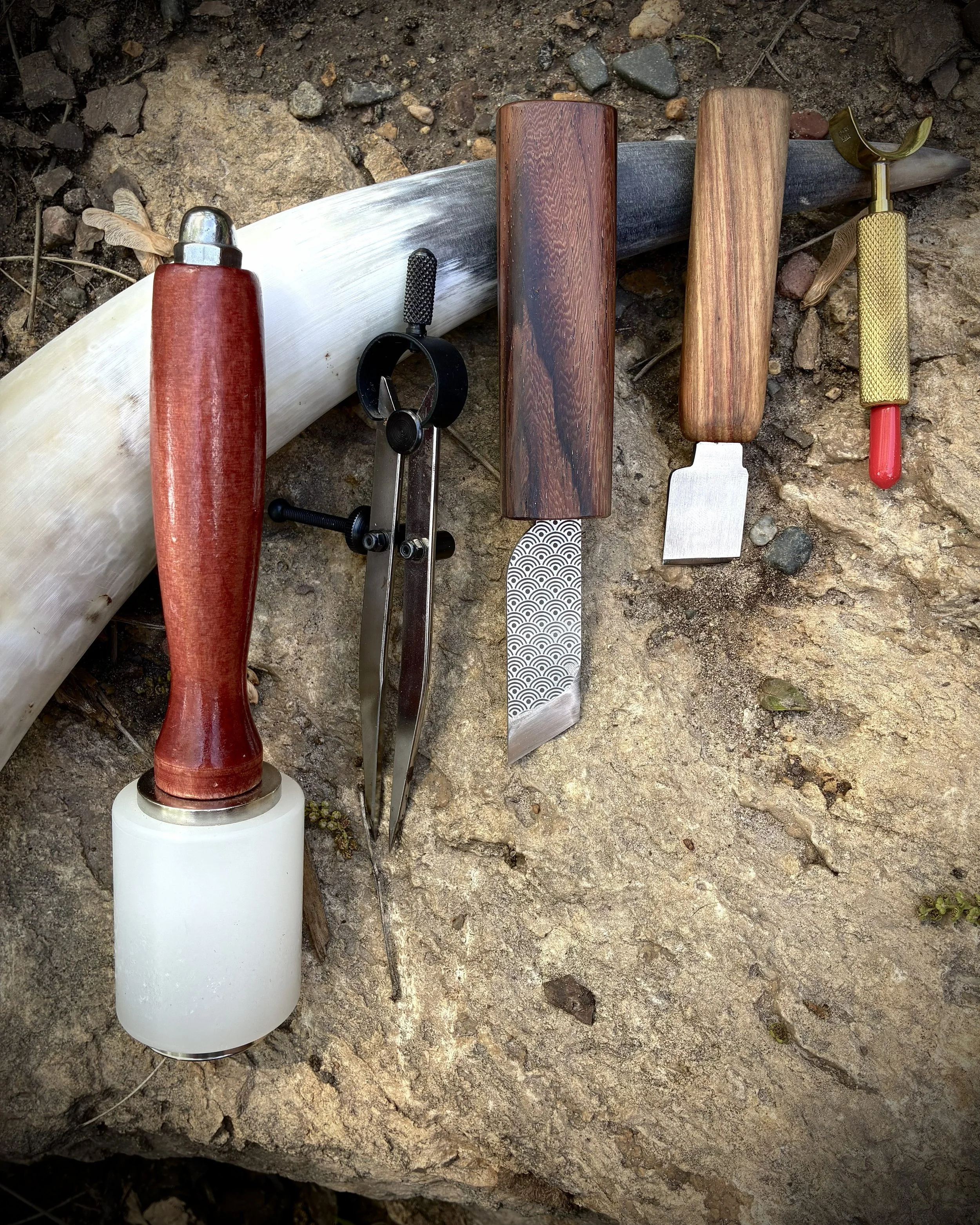 Classic leatherworking tools, displayed on a rock, propped up on a natural bull horn.
