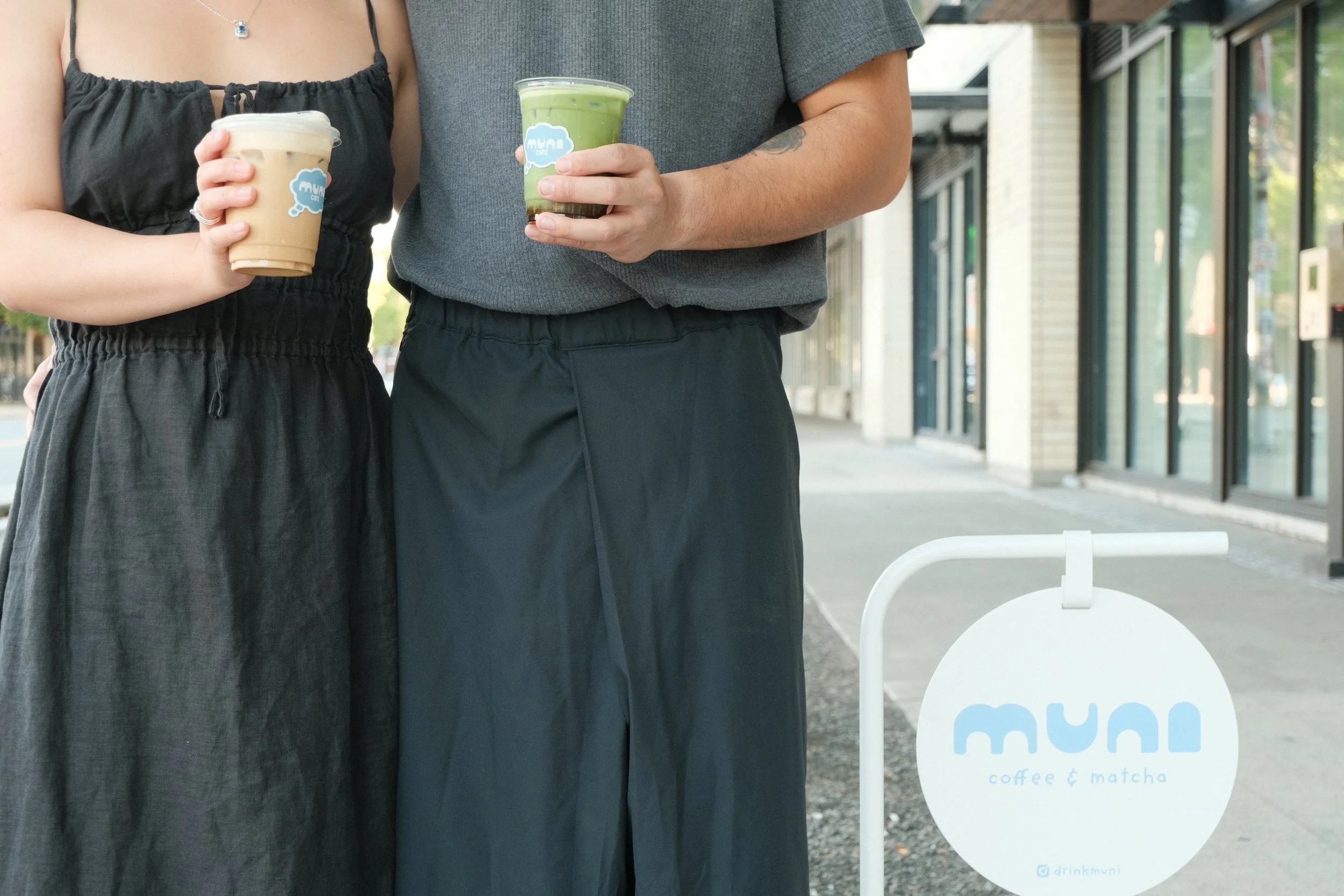 Two people holding drinks outside a cafe with a sign reading 'muni coffee & matcha'.