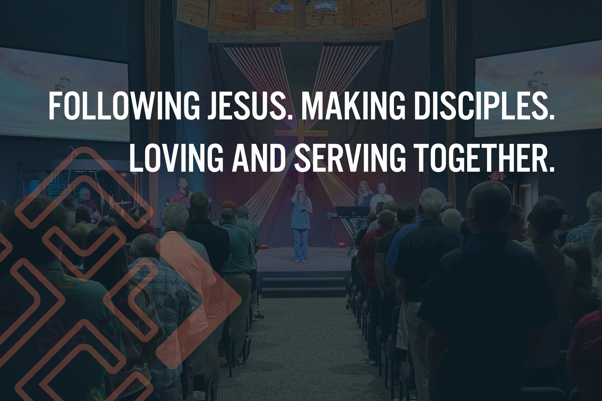 A congregation gathered inside a church listening to a speaker on stage. The background features a large illuminated cross and colorful lighting.
