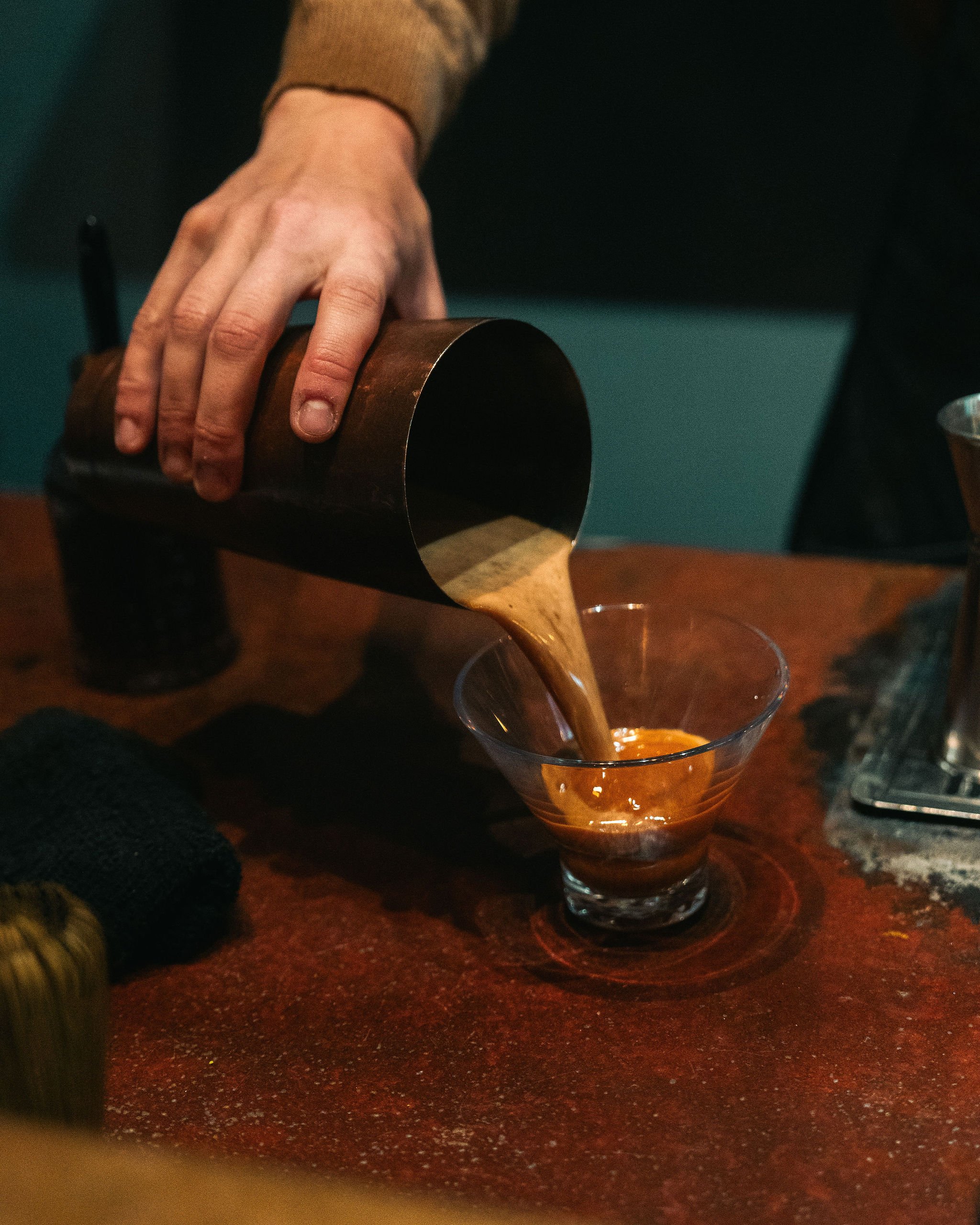 A person pouring a coffee drink from a shaker into a glass cup.