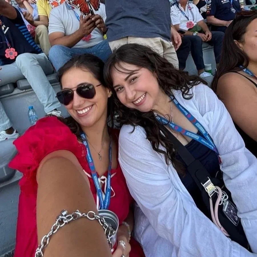 Two women smiling and taking a selfie at an outdoor event, with many other people in the background.