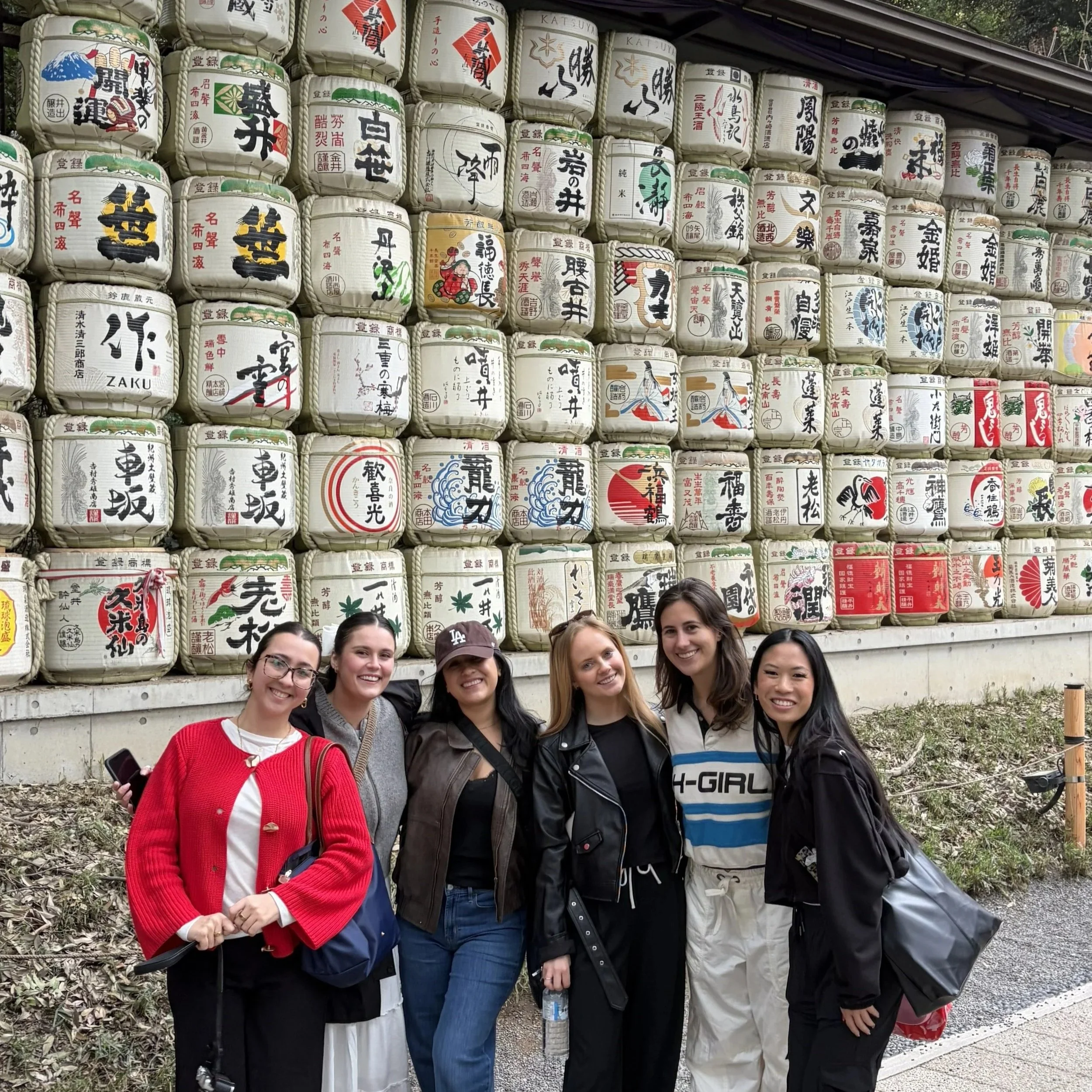 Group of women smiling and posing in front of a wall of traditional Japanese sake barrels.