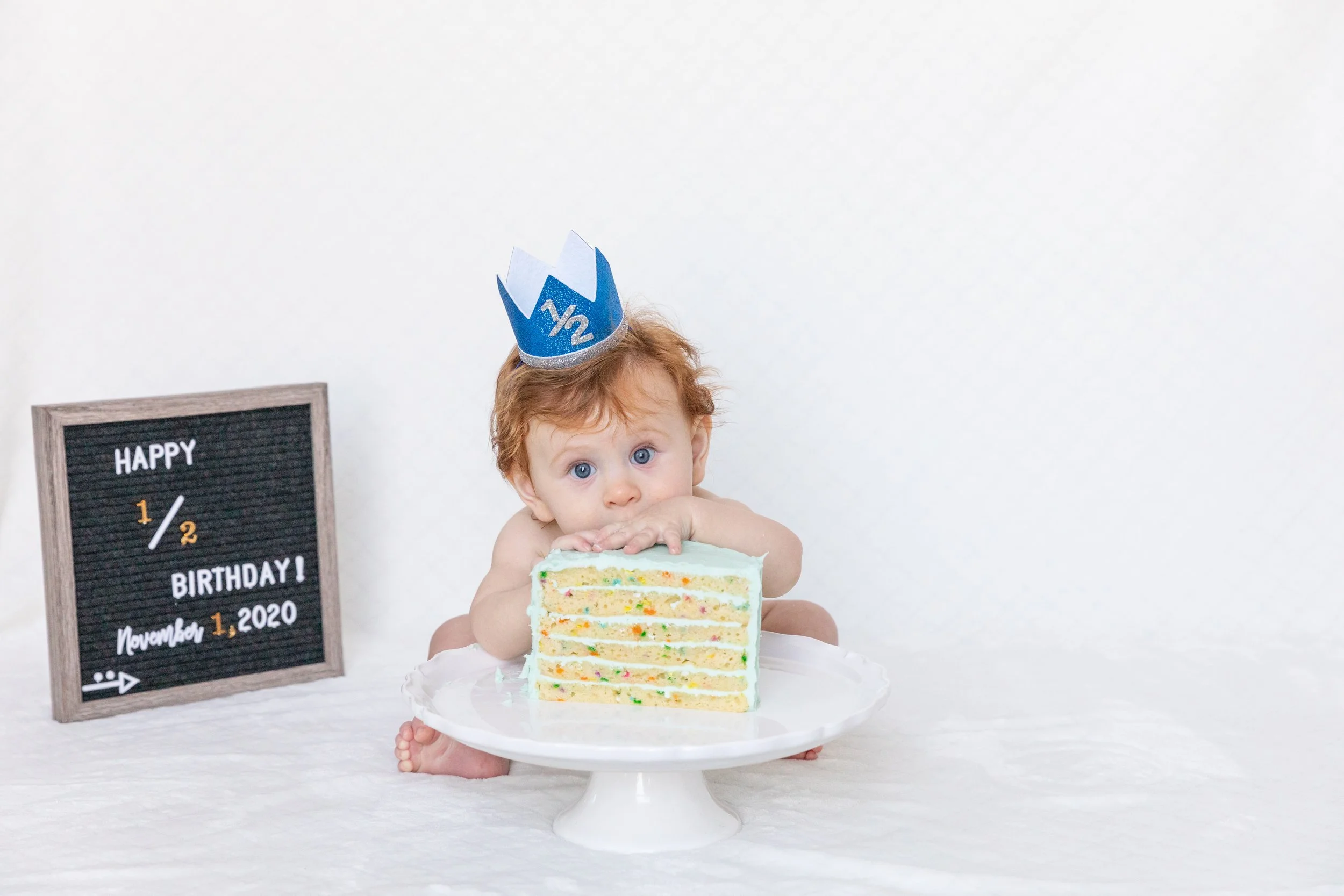 Half-birthday baby photography session capturing a joyful cake moment and playful expressions.