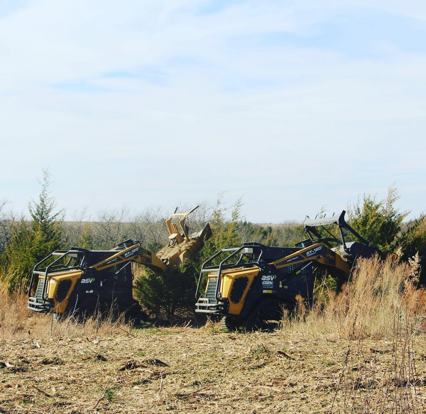 Two small construction vehicles in a field with trees in the background and a clear sky
